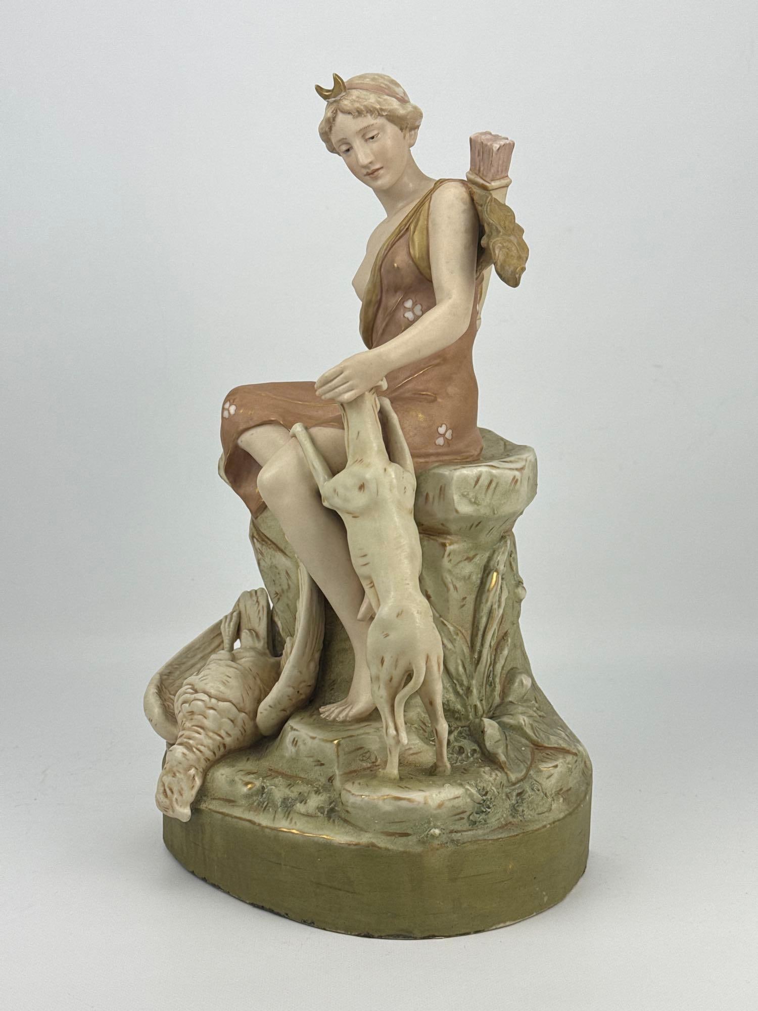 ROYAL DUX BOHEMIA DIANA THE HUNTRESS PORCELAIN FIGURINE: *Polychrome porcelain sculpture depicting the seated Roman goddess with a crescent moon tiara, quiver of arrows, hound, and hunted game bird, Approximate Dimensions: 15.25” h x 9.5”w x 7&r