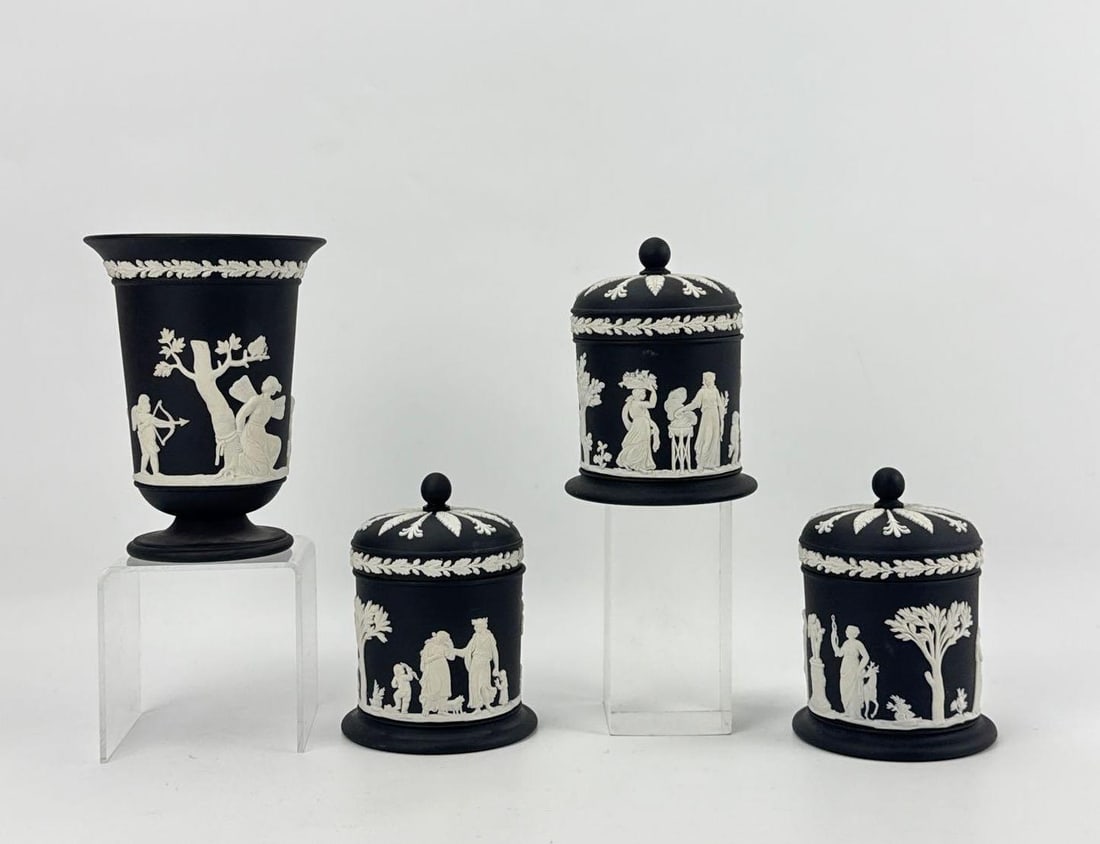 COLLECTION OF FOUR WEDGWOOD BLACK BASALT JASPERWARE TOILETRIES JARS AND VASE: Group of four 20th-century English matte black stoneware basalt vessels ornamented with classical white slip-cast relief figures, including three matching lidded canisters and one footed urn-form vase