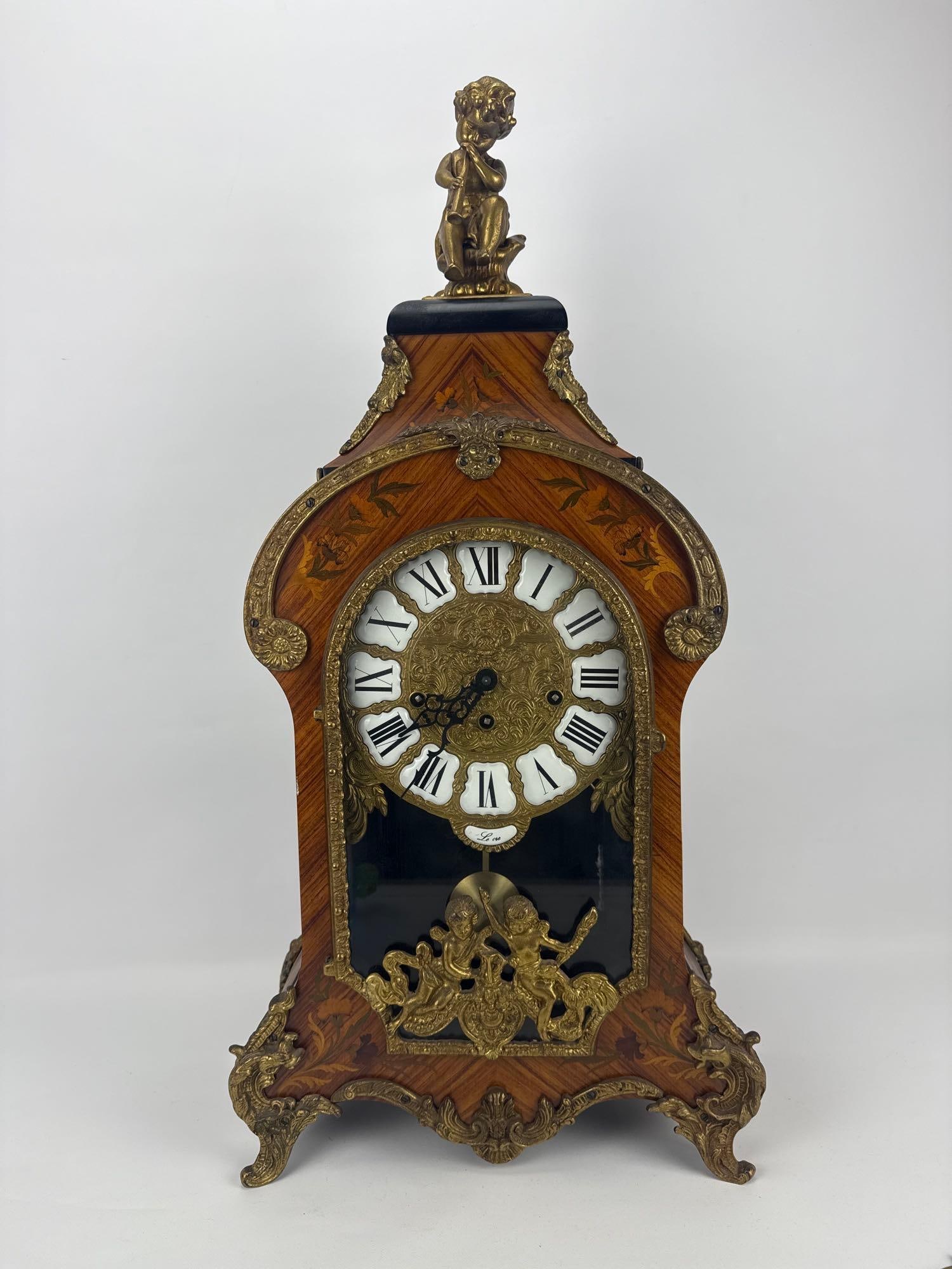 VINTAGE LE ORE ITALIAN LOUIS XV STYLE ORMOLU MANTEL CLOCK: Vintage Italian Louis XV style bracket mantel clock with an inlaid wood case, ornate gilt bronze ormolu mounts, Roman numeral porcelain cartouche dial, and a figural cherub finial Approximate Dimensio