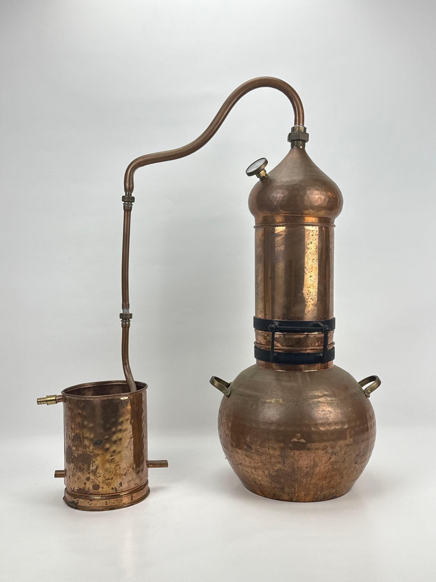 HANDCRAFTED COPPER ALEMBIC MOONSHINE STILL: Handcrafted hammered copper dual-vessel whiskey distiller with integrated column, swan neck piping, condenser unit. Approximate Dimensions: 29.5” H X 24” W X 11.5” D Artist or Maker: