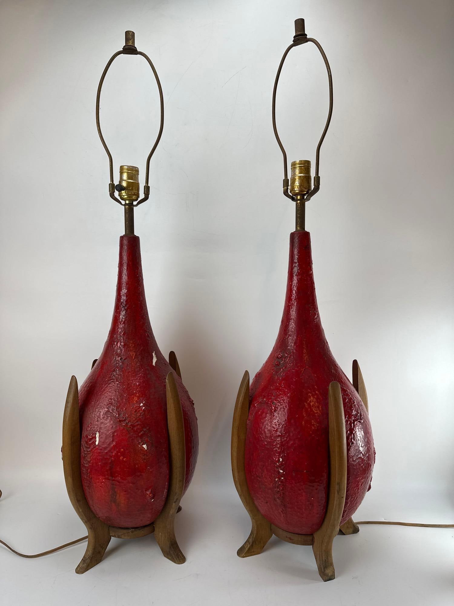 PAIR OF VINTAGE MID-CENTURY LAVA GLAZE ROCKET LAMPS: *A pair of 1960s mid-century modern tear-drop ceramic table lamps featuring a vibrant, highly textured red "fat lava" or volcanic drip glaze, each cradled on a sculpted four-legged walnut wood