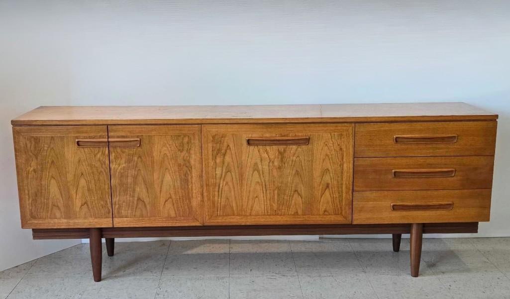 MID CENTURY MODERN DANISH TEAK LONG JOHN CREDENZA SIDEBOARD: Danish modern low-profile teak wood entertainment console buffet with three sliding cabinet doors opening to interior shelving and a bank of shallow drawers on tapered legs Approximate Dimensions: 28.