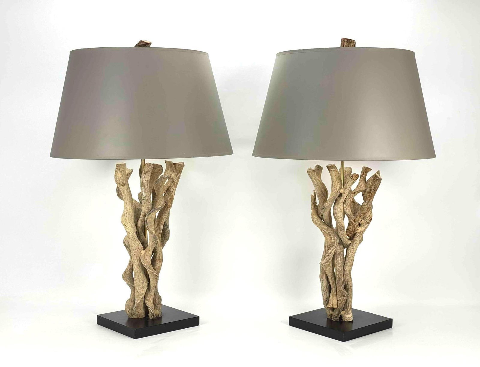 PAIR OF SIGNED JAMIE YOUNG COASTAL DRIFTWOOD TABLE LAMPS WITH TAUPE SHADES: A pair of coastal-style table lamps constructed with natural intertwined sculptural driftwood bases resting on square dark plinths, completed with tapered taupe shades and wood finials. Approximate Di