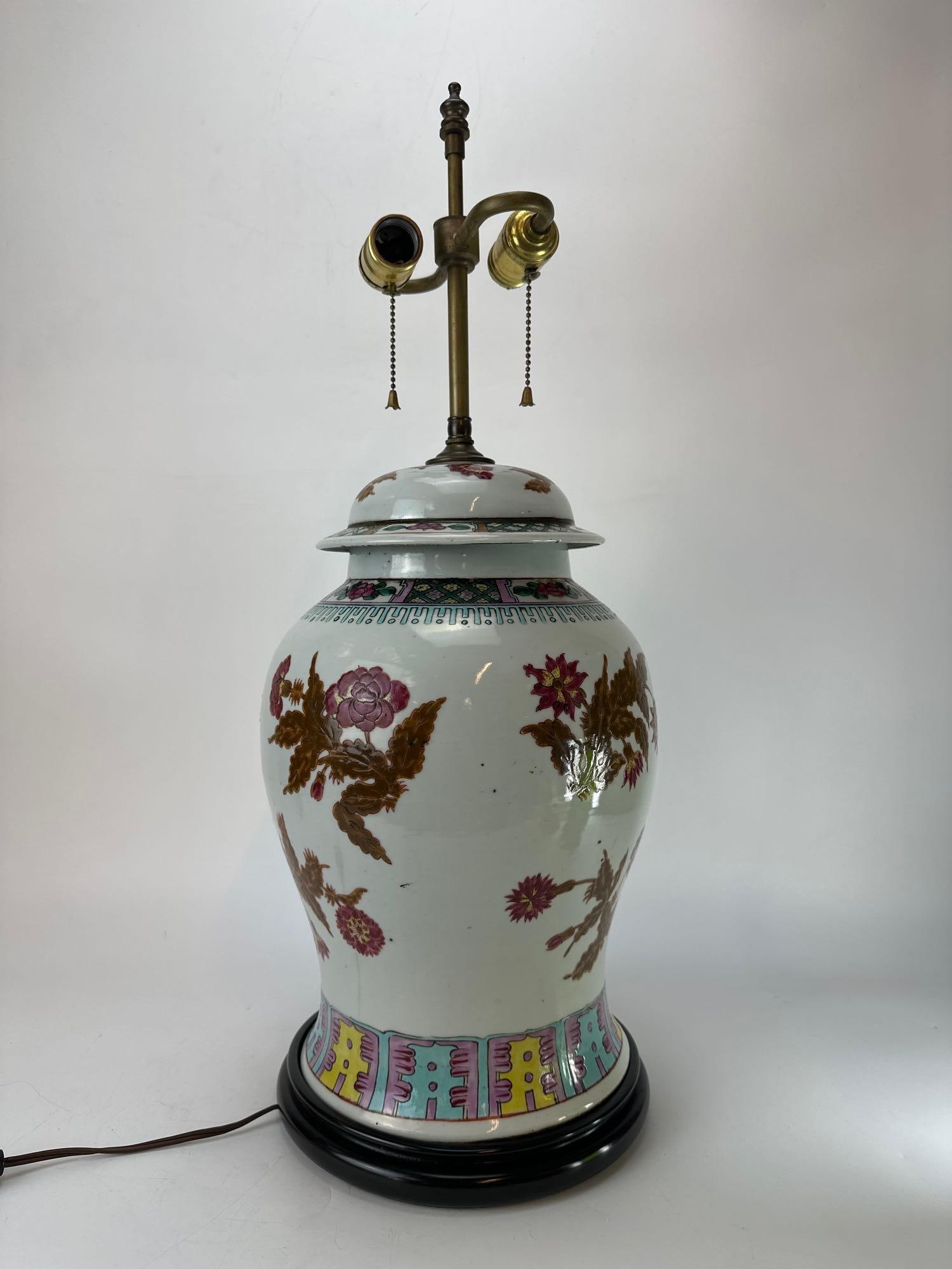 20TH CENTURY CHINESE FAMILLE ROSE GINGER JAR TABLE LAMP: A Chinese famille rose porcelain ginger jar mounted as a table lamp on a wooden base decorated with hand painted flowers and scrolling foliage. Approximate Dimensions: 27” H X 11" Dia. Artis
