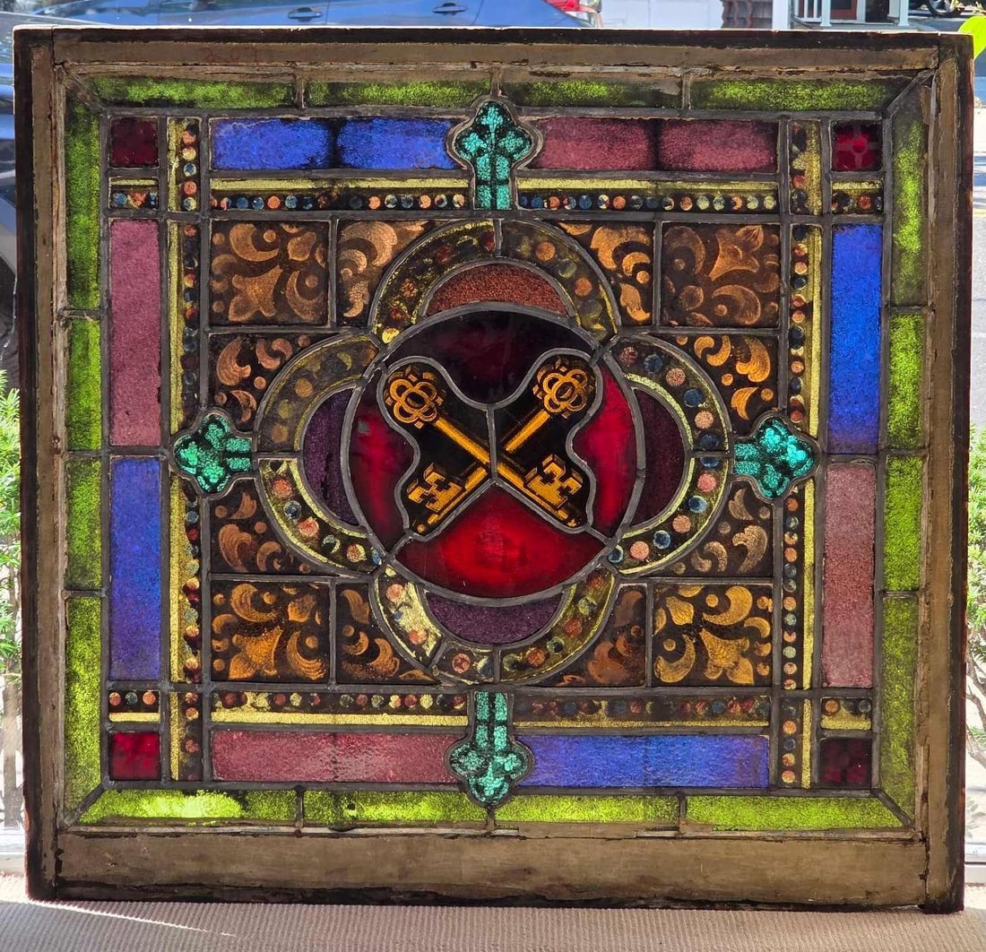 AMERICAN ANTIQUE LEADED STAINED GLASS CHURCH WINDOW WITH CROSSED KEYS (1 0f 4): A religious leaded stained glass architectural window panel depicting the crossed Keys of St. Peter within a colorful geometric and scrollwork border, housed in its original wooden frame. Approximate 