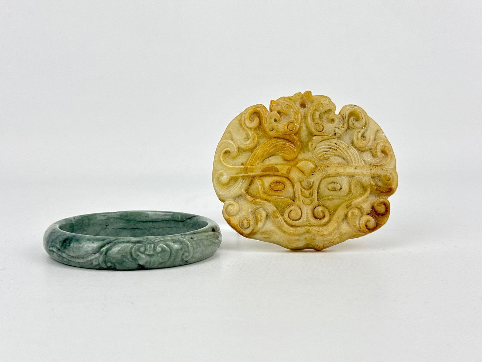 CHINESE ANTIQUE CARVED JADE ARCHITECTURAL TAOTIE MASK PLAQUE AND JADEITE BANGLE: A pair of antique Chinese carved jade elements consisting of a thick, pierced nephrite jade openwork plaque sculpted as an archaic Taotie monster mask or stylized bi disc alongside a continuous moss-o