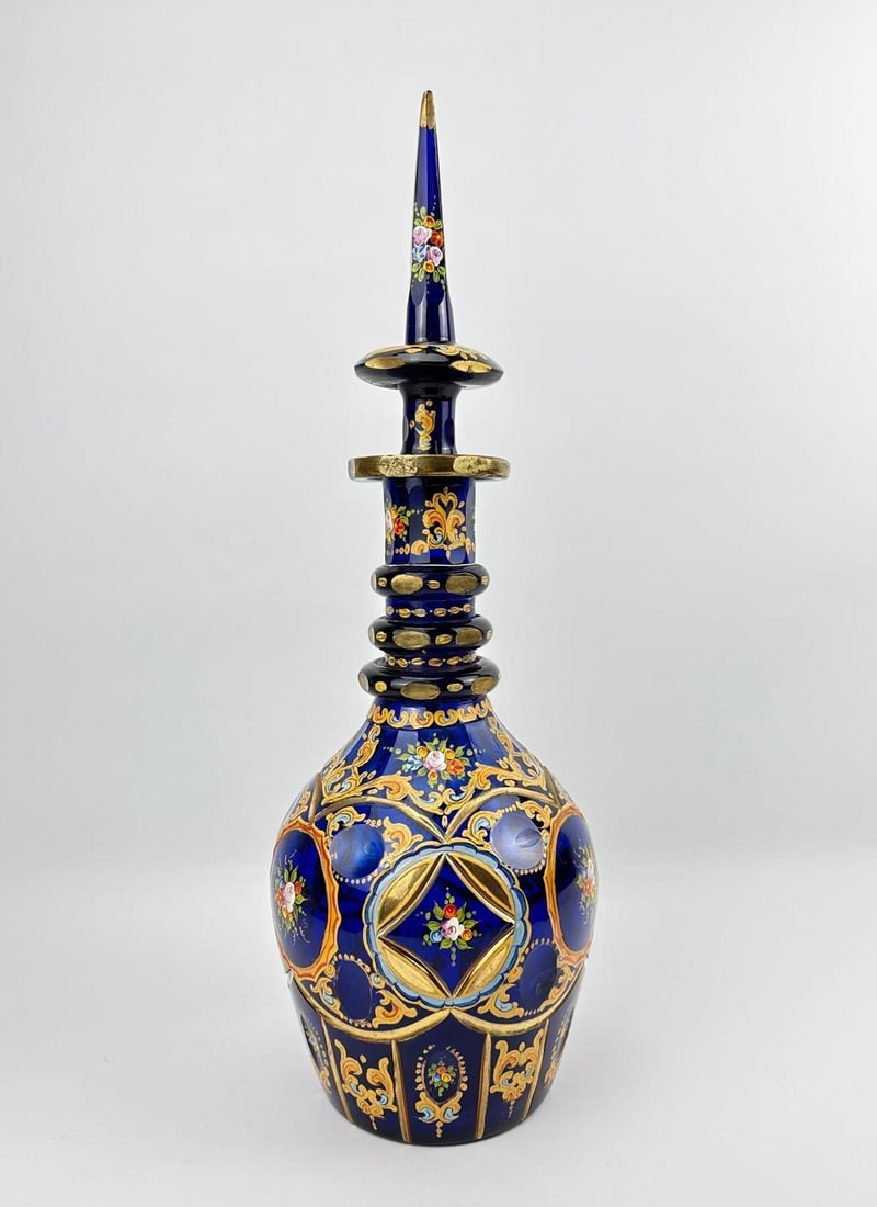 BOHEMIAN PERSIAN DARK BLUE DECANTER: *An elongated, cobalt blue glass decanter ornamented with heavily gilded scrollwork, painted Persian paisley floral medallions, a triple-ring neck, and a matching spire-form stopper. Approximate Dimen