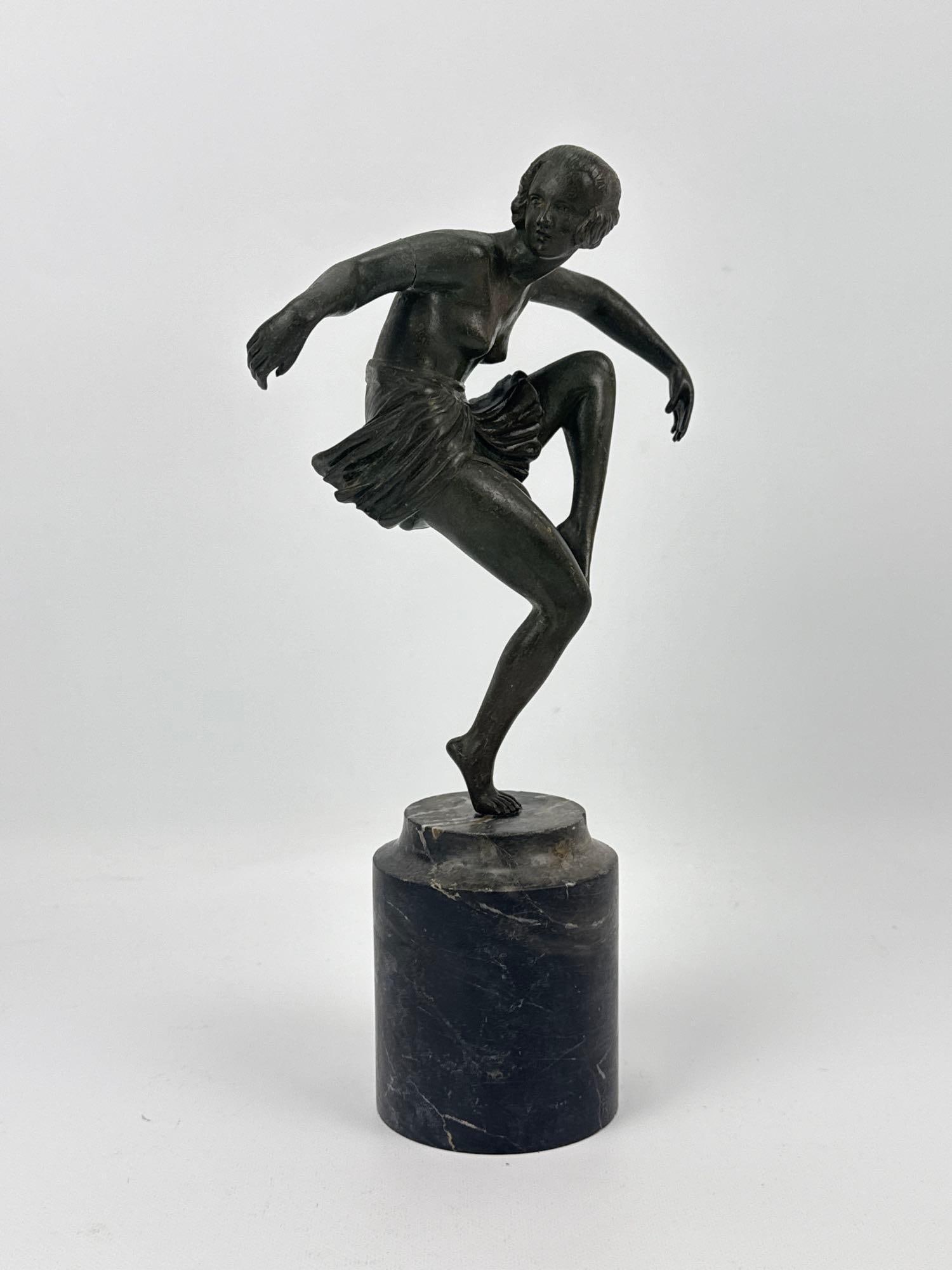 ANTIQUE ART DECO PATINATED BRONZE STUDY OF A DANCER ON MARBLE BASE: *Bronze figural sculpture capturing a stylized dancer poised mid-motion on one leg, complete with a flowing pleated skirt and an organic dark patina, elevated on a tall cylindrical veined black marble