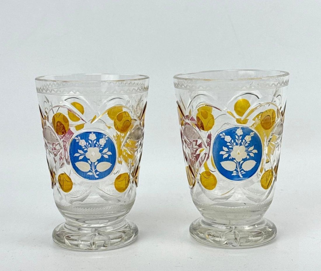 TWO ANTIQUE 19TH CENTURY BOHEMIAN BIEDERMEIER AMBER FLASHED GLASS FRIENDSHIP BEAKERS: Two nineteenth-century European amber stained glass tumblers decorated with blue enamel medallions and intricate wheel-cut geometric patterns Approximate Dimensions: 4.5” H X 3” Dia. Artis