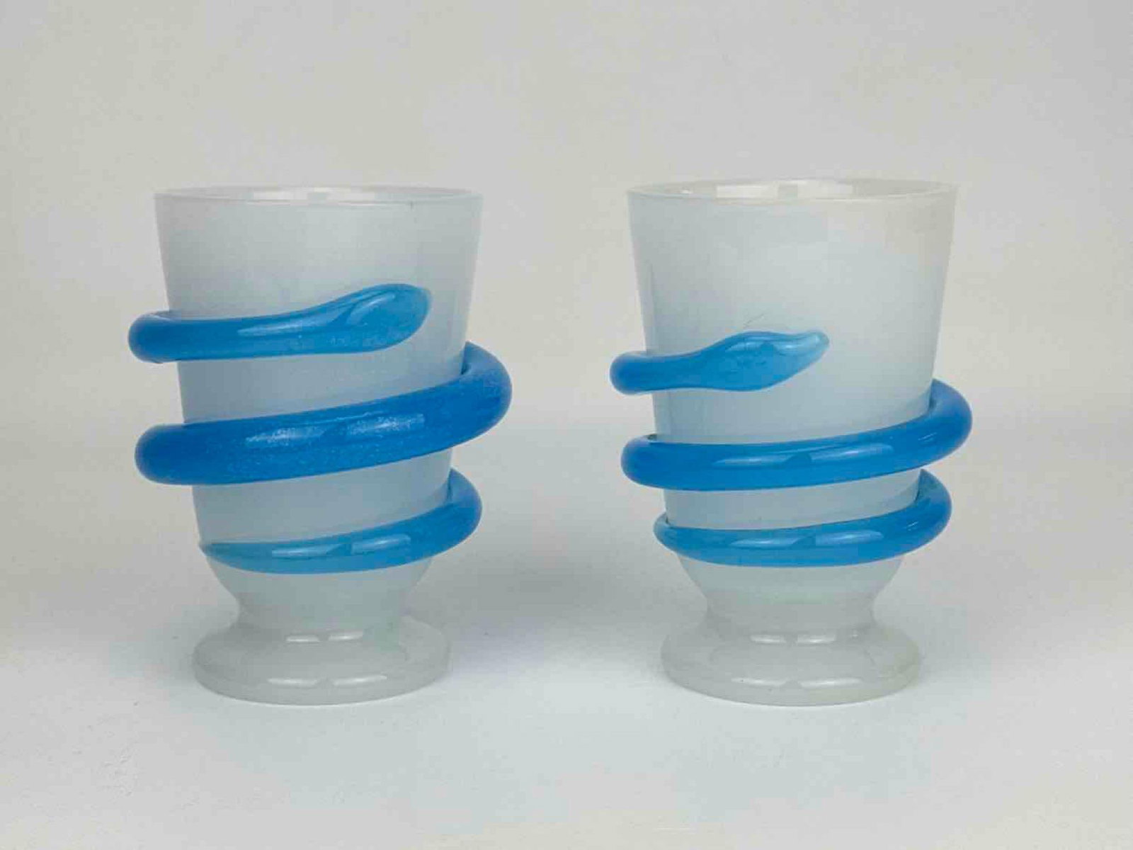 PAIR OF ANTIQUE BOHEMIAN OPALINE GLASS TUMBLERS WITH APPLIED COILED SNAKES: Two semi-translucent white milk glass footed beakers featuring an applied bright blue glass serpent coiled around the body Approximate Dimensions: 5” H X 3.5” W X 3” Dia. Art