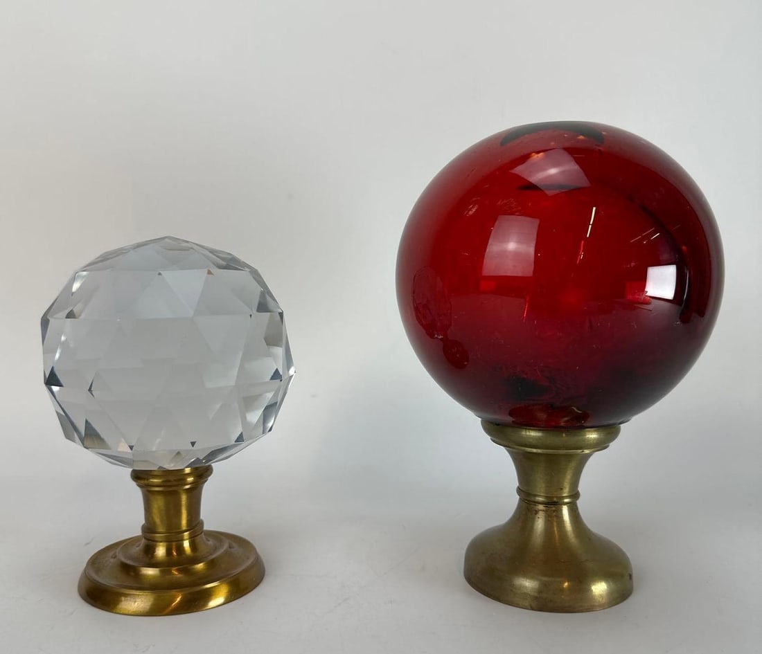 TWO LARGE MOUNTED ART GLASS ORBS / SPIRIT BALLS - ONE FACETED, ONE RED SMOOTH: An assortment of two large art glass crystal accent pieces orbs/spirit balls. The lot features one clear glass orb with geometric hand-cut faceted patterning, and one striking smooth glass sphere in