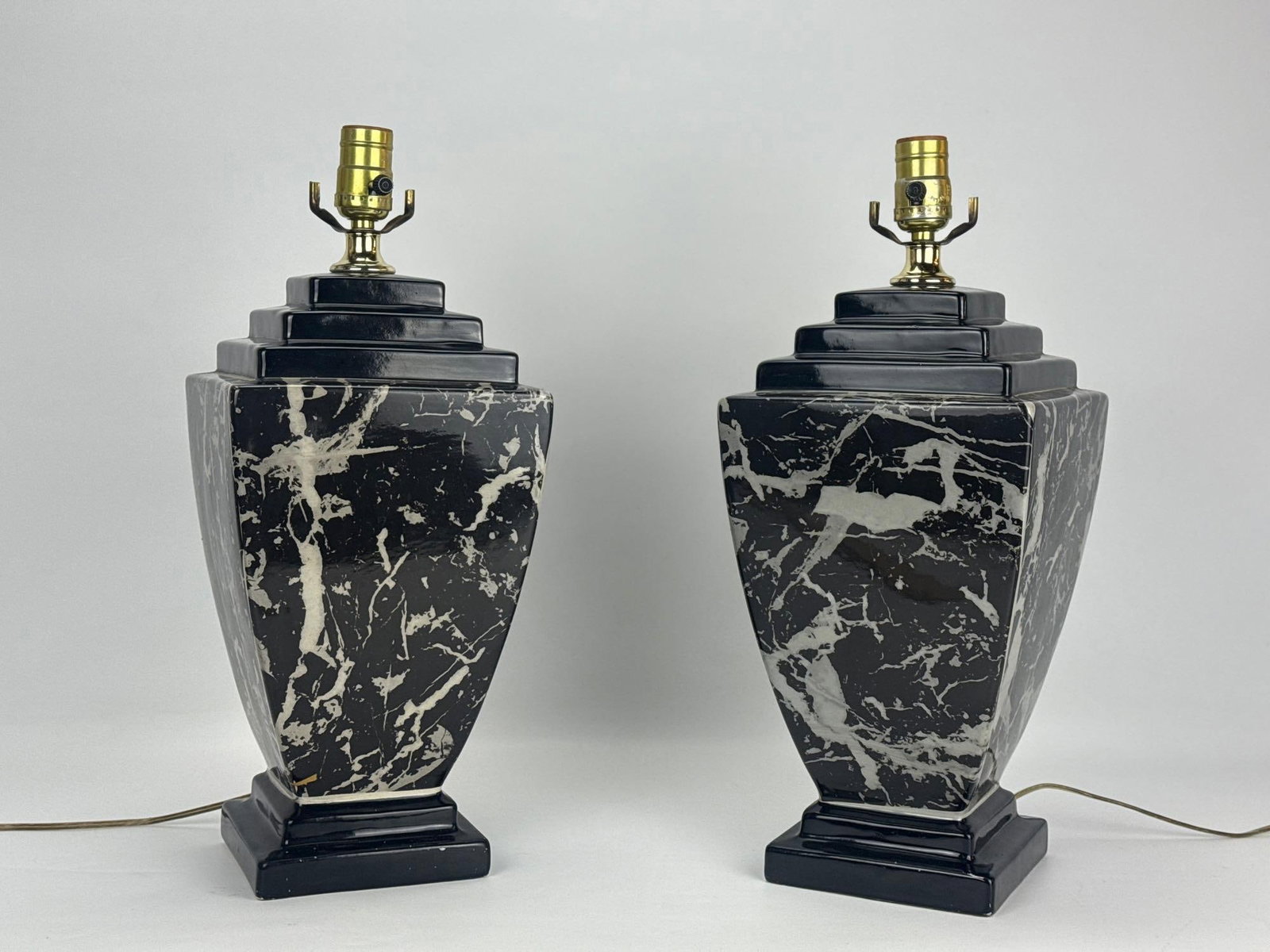 PAIR OF VINTAGE BLACK FAUX MARBLE CERAMIC TABLE LAMPS: Pair of vintage neoclassical style ceramic table lamps shaped as square baluster urns with tiered stepped lids finished in a glossy black faux marble and white veined onyx glaze. Approximate