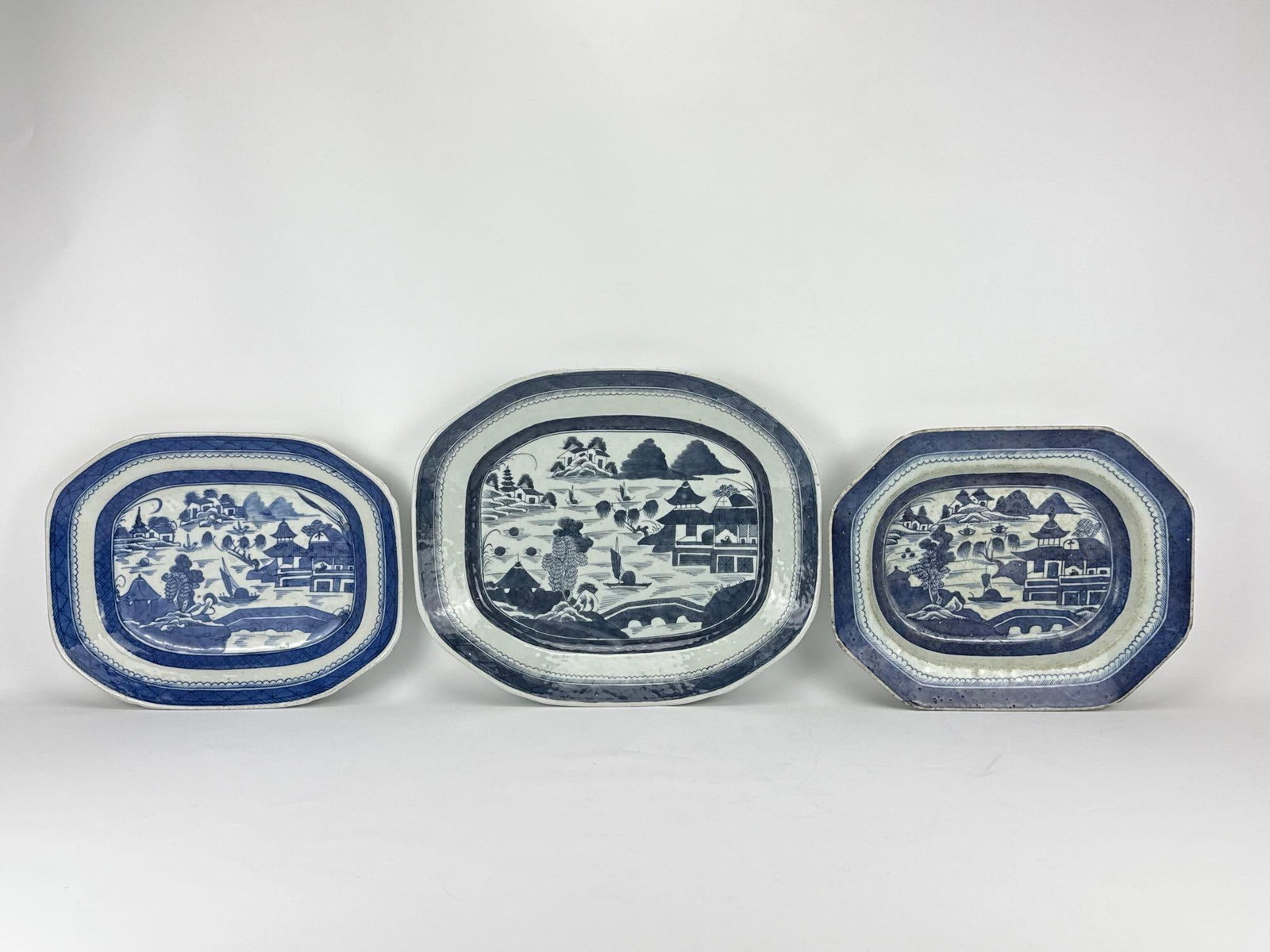 19TH-C CHINESE EXPORT BLUE CANTON PORCELAIN PLATTERS LOT OF 3 (ONE SIGNED): Set of three antique graduated octagonal deep serving platters in underglaze blue and white Chinoiserie landscape motif including one signed piece. Approximate Dimens