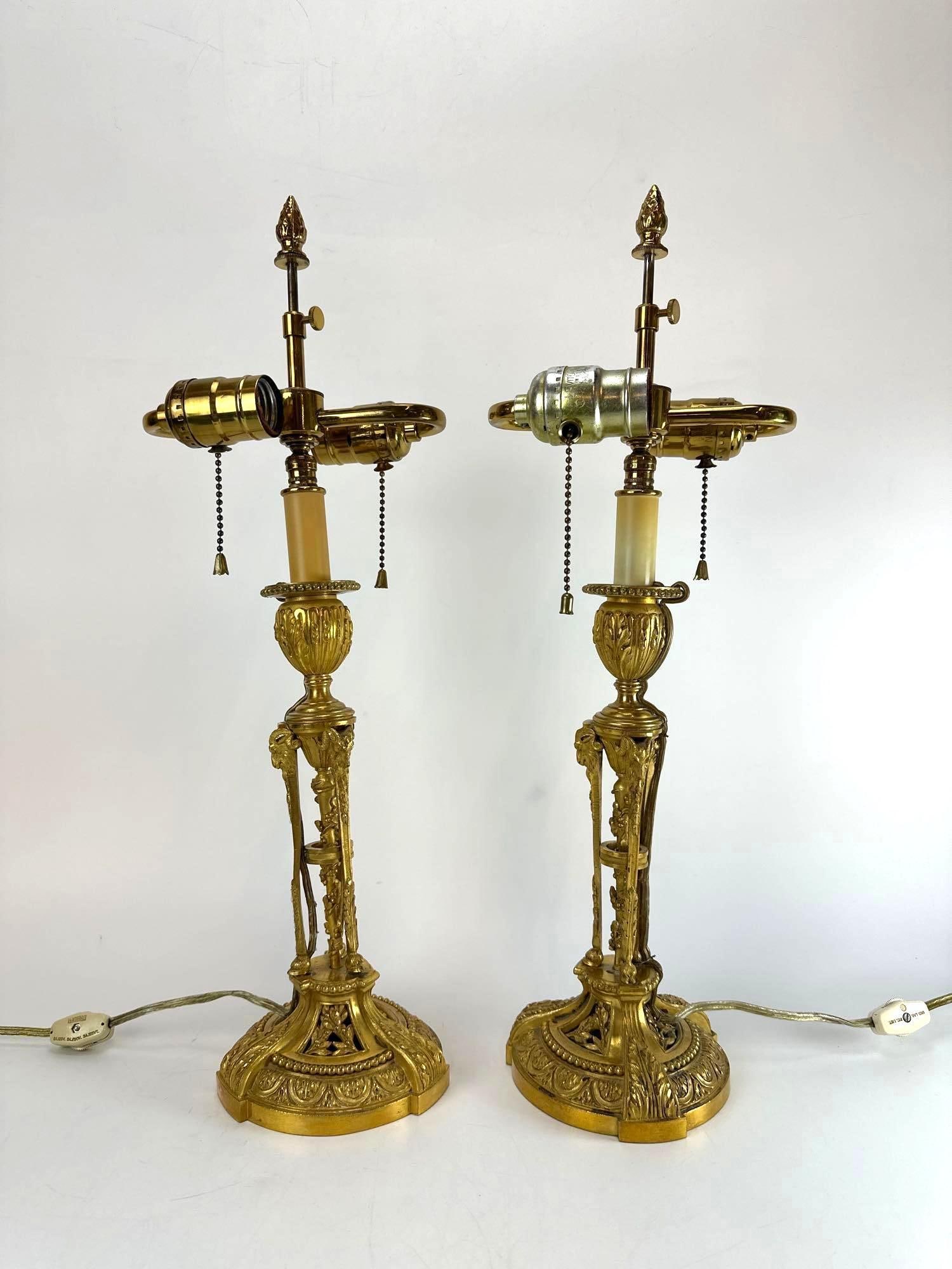 PAIR OF FRENCH NEOCLASSICAL STYLE BRASS BOUILLOTTE TABLE LAMPS: A pair of cast brass bouillotte-style candlestick table lamps with ornate acanthus leaf columns, openwork tripod bases. Please note: one lamp is comprised and leans. Approximate Dimensions: 20"H x