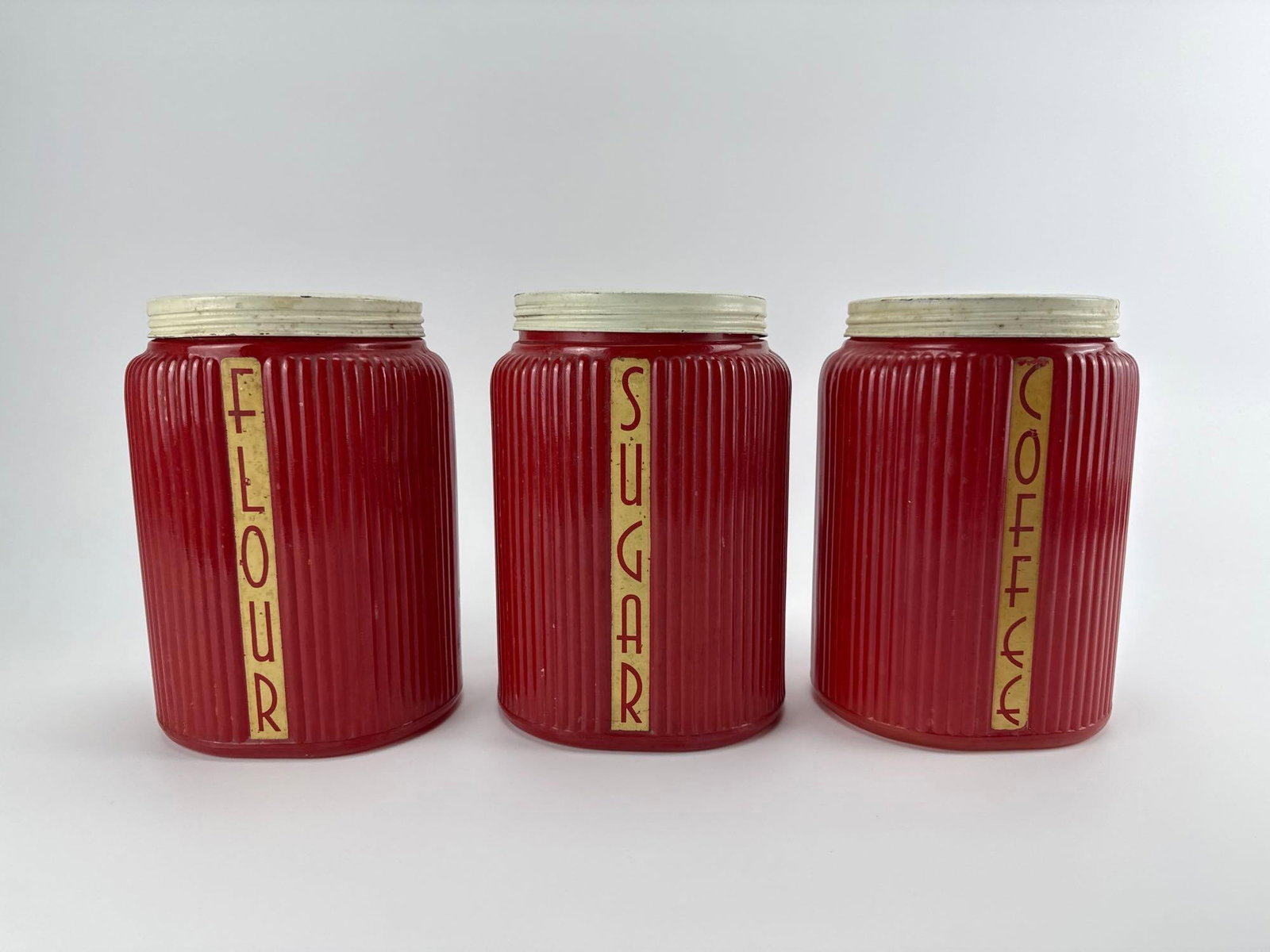 VINTAGE OWENS-ILLINOIS GLASS CO. DEPRESSION ERA RED RIBBED CANISTER SET OF 3 COFFEE SUGAR FLOUR: Three-piece red ribbed glass kitchen storage set with cream metal lids and vertical lettering decals for coffee, flour, and sugar Approximate Dimensions: 6”’x 5” x 8” tall Artist o