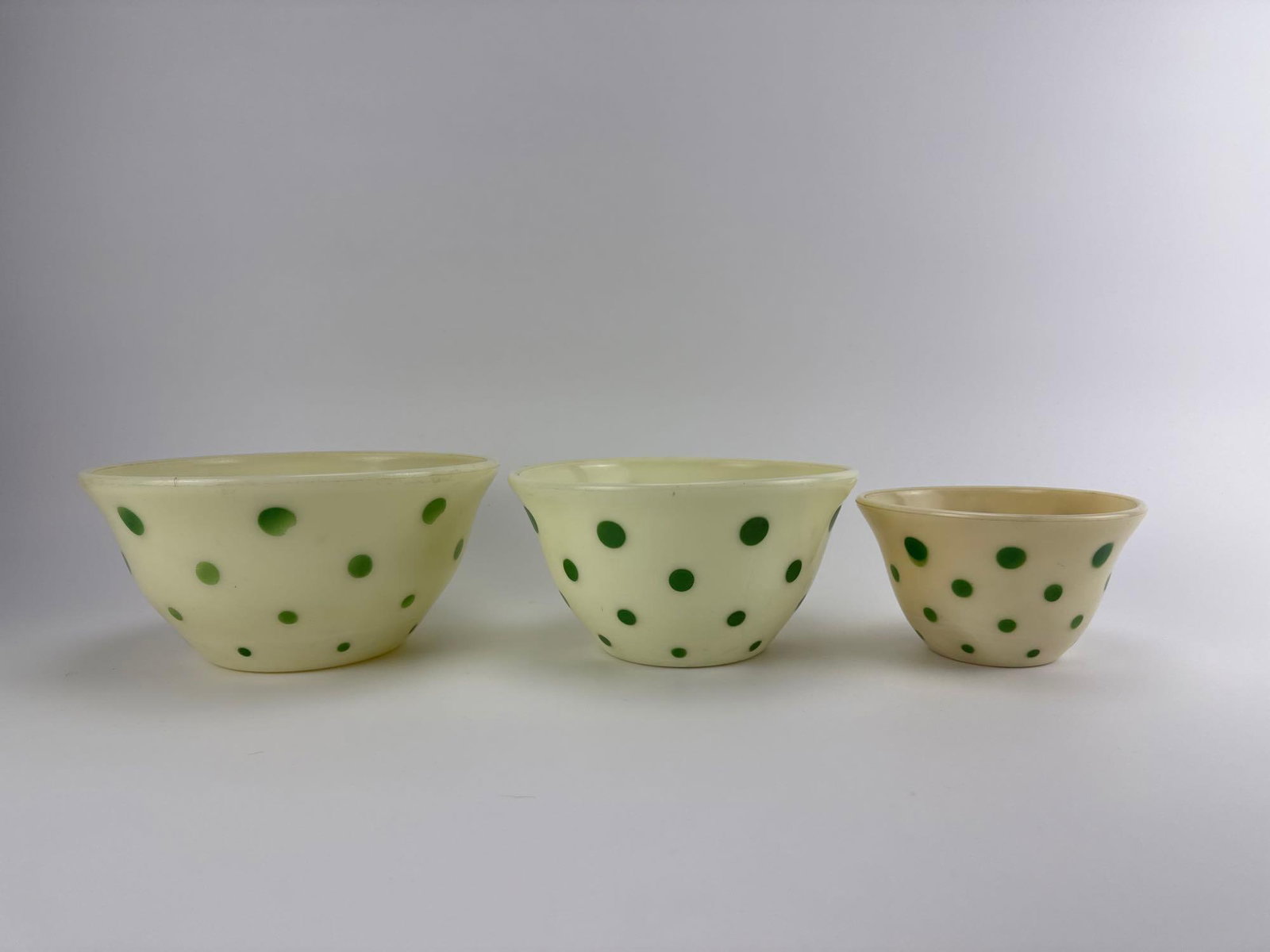 THREE RARE VINTAGE MCKEE POLKA DOT MILK GLASS NESTING MIXING BOWLS: Three-piece antique 1930s milk glass nesting kitchen mixing bowl set adorned with a red polka dot pattern, featuring a largest bowl of nine-inch diameter. Approximate Dimensions: largest bowl 9”