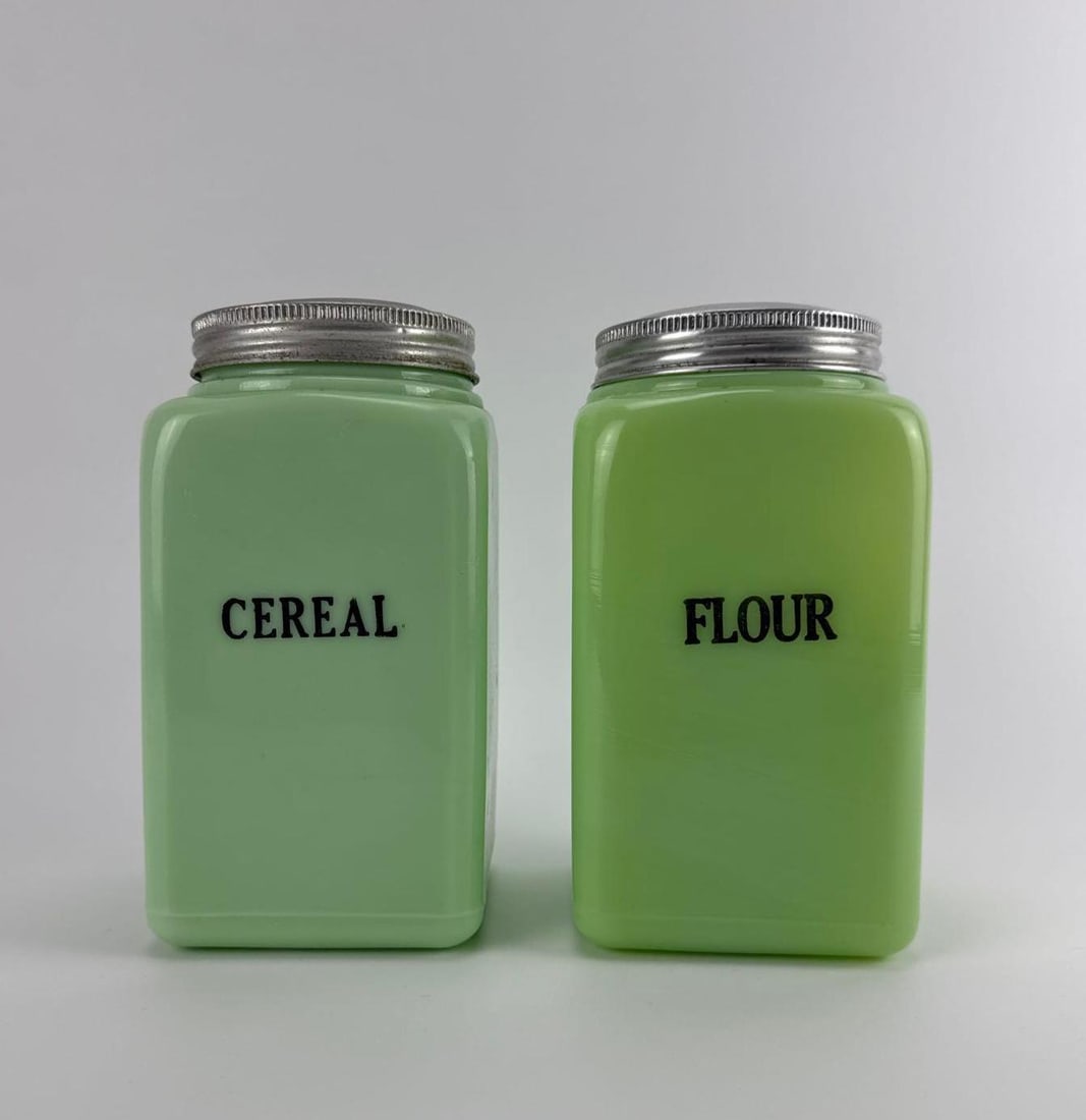 PAIR OF VINTAGE MCKEE GLASS CO. JADEITE SQUARE KITCHEN CANISTERS WITH ALUMINUM LIDS: Pair of antique 1930s opaque green uranium jadeite glass square kitchen canisters with original screw-on metal lids labeled for cereal and flour. Approximate Dimensions:4” x 4” x 7.5&rdquo