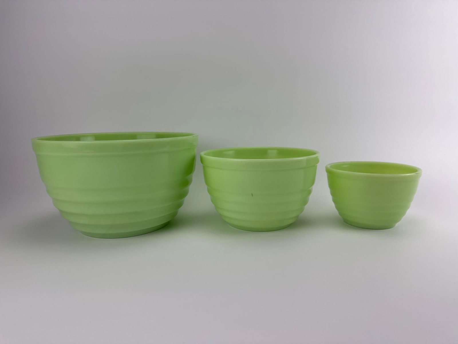 THREE VINTAGE JEANNETTE GLASS CO. JADEITE CONCENTRIC RING NESTING MIXING BOWLS: Three-piece antique 1930s opaque green uranium jadeite glass nesting kitchen mixing bowl set with embossed concentric ring borders. Approximate Dimensions: Largest 6” tall x 9.75” dia Arti