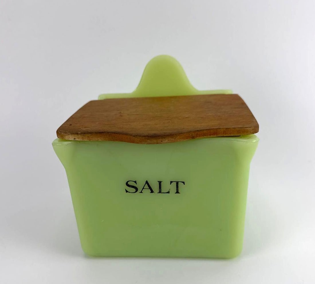 RARE VINTAGE JEANNETTE GLASS CO. JADEITE GLASS SALT BOX WITH ORIGINAL WOODEN LID: Antique 1930s opaque green uranium jadeite glass wall-hanging salt cellar with black typography and original fitted wooden lid. Approximate Dimensions: 5”x 5” x 5.5” t Artist or
