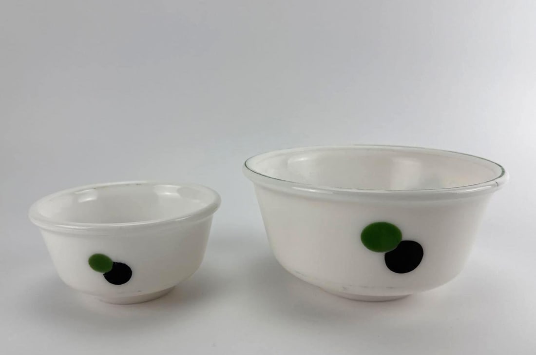 PAIR OF VINTAGE OPAQUE WHITE GLASS GREEN AND BLACK POLKA DOT NESTING MIXING BOWLS: Pair of vintage mid-century semi-opaque white milk glass nesting kitchen bowls decorated with overlapping green and black double polka dots. Approximate Dimensions: Larger 3.5” t x 7.5” di