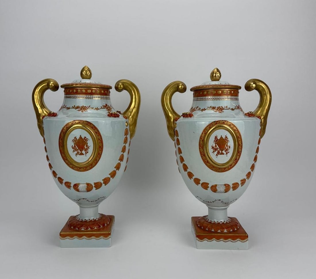 PAIR OF VINTAGE ITALIAN PORCELAIN CAPODIMONTE STYLE LIDDED URNS: Pair of mid-century neoclassical style footed porcelain mantel jars with lids adorned with gilded scroll handles, iron-red swag details, and central oval medallions depicting classical urn motifs on s