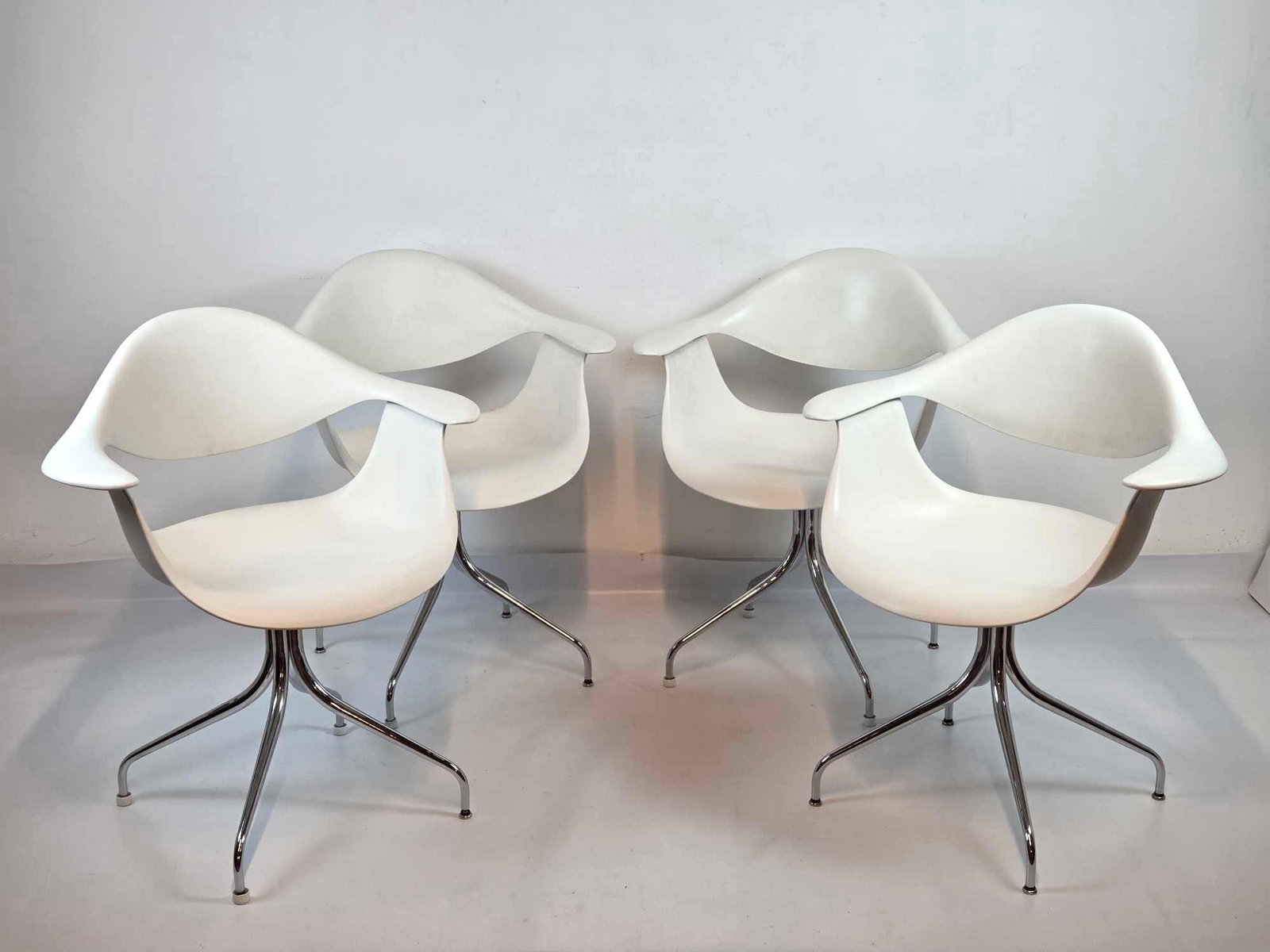 SET OF FOUR GEORGE NELSON SWAG LEG ARMCHAIRS FOR HERMAN MILLER: A set of four, mid-century modern molded white fiberglass shell chairs on chrome-plated steel swagged legs. Approximate Dimensions: 32"H x 28"W x 20"D Artist or Maker: George Nelson for He