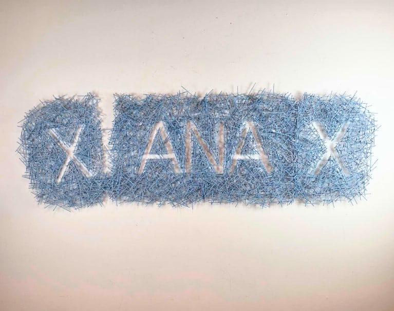ROY BRAEGER DIMENSIONAL ART PIECE "XANAX" TAB PILL: Large-scale 3D blue typographical relief sculpture depicting a Xanax tablet made of thousands of bamboo rods of varying lengths,. Approximate Dimensions: 24" H X 72" W Artist or Maker: Roy Bra