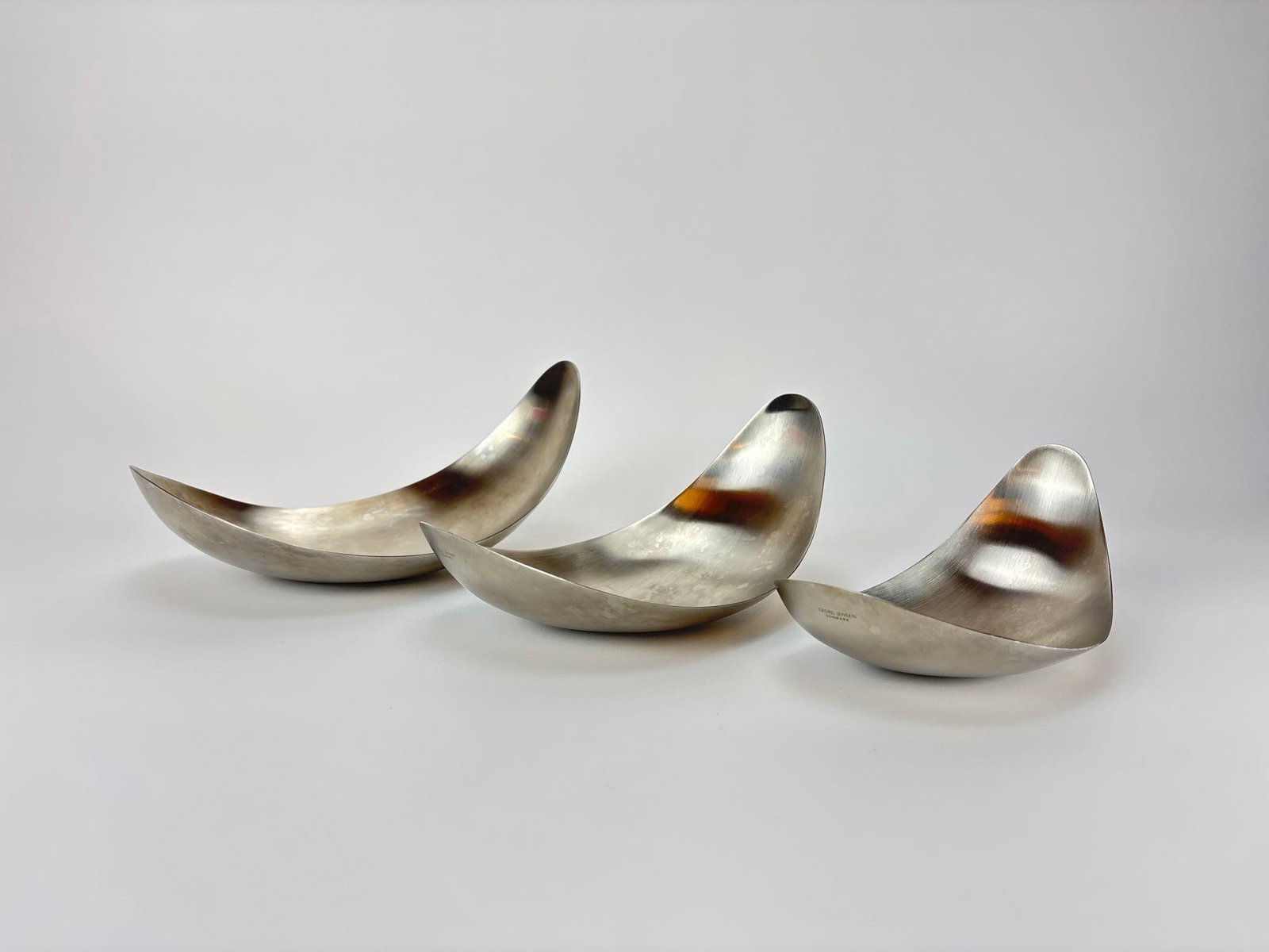 GEORG JENSEN DANISH MODERN MATTE STAINLESS STEEL "LEAF" NESTING CRESCENT BOWLS TRIO: Trio of Danish Modern matte-finished stainless steel nesting serving bowls designed in fluid crescent forms, stamped with Georg Jensen maker mark to base. Approximate Dimensions: LARGEST 4" H X 5&