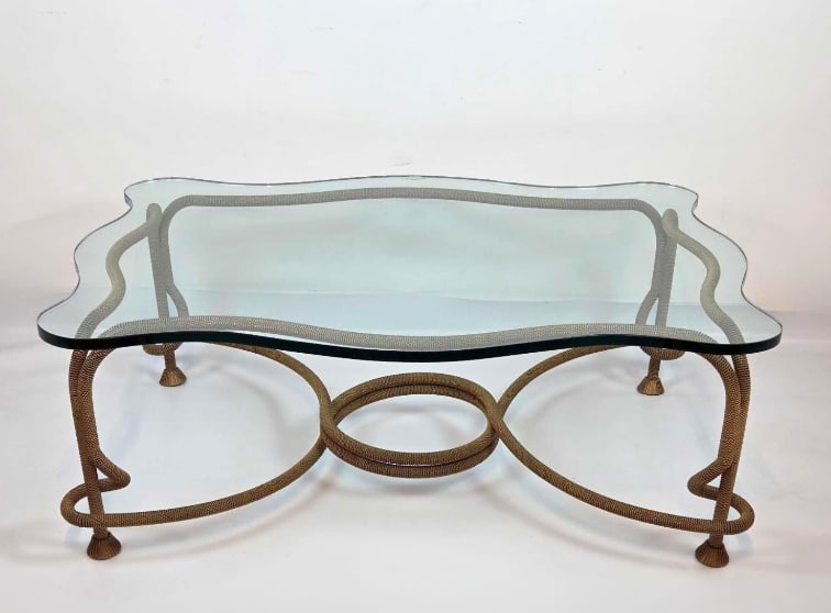 EMILIO REY VINTAGE GILT BRONZE CORD GLASS TOP COFFEE TABLE: Gilt bronze coffee table with a twisted rope-and-tassel cord base joined by an interlocking oval stretcher, topped with a shaped glass surface showing a small chip to one corner edge. Approximate Dime