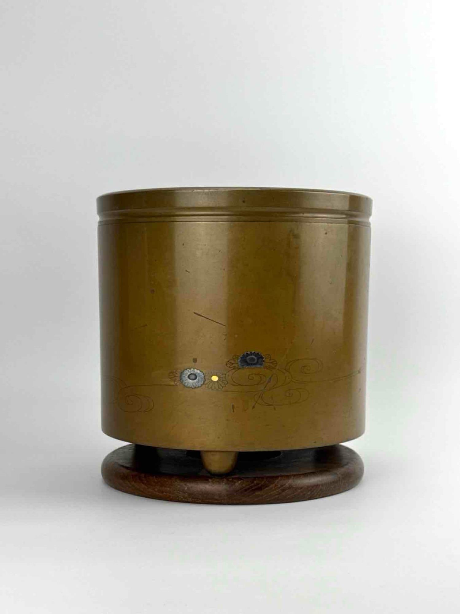 ANTIQUE JAPANESE MIXED-METAL INLAID BRONZE HIBACHI ON WOOD BASE: Cylindrical Japanese bronze or copper hibachi (brazier) resting on integrated feet over a custom fitted wooden base, decorated with incised wave motifs and fine mixed-metal soft-metal inlaid chrysanth