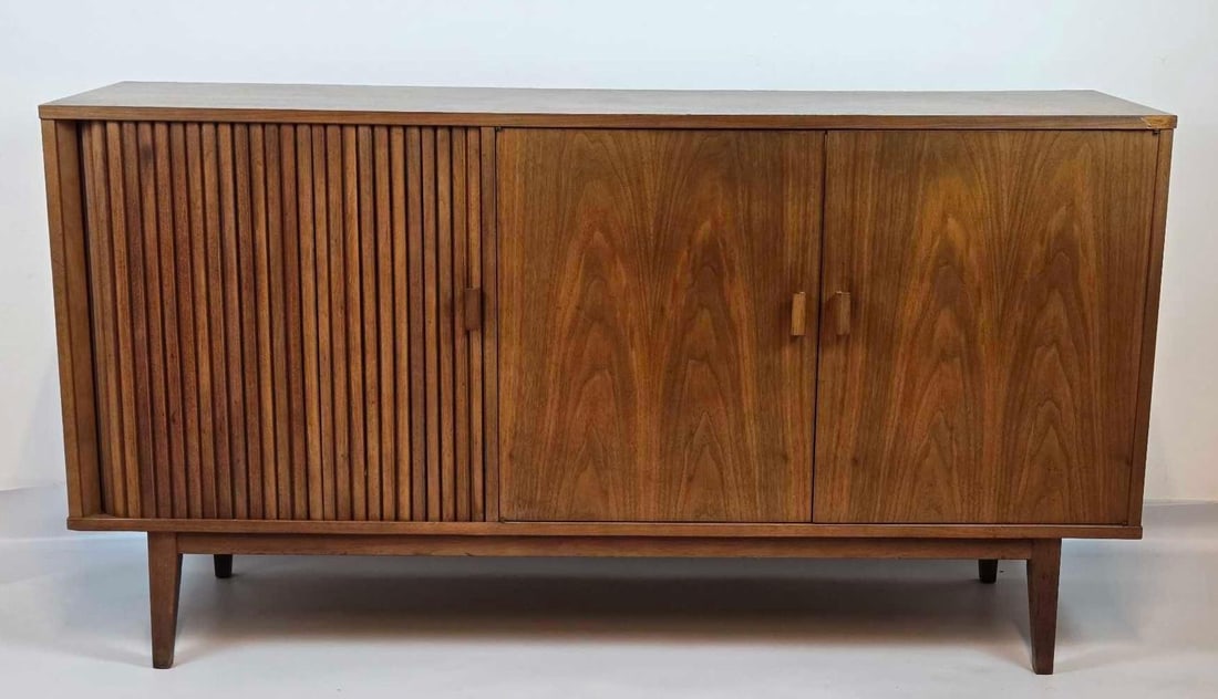 MILO BAUGHMAN STYLE MID CENTURY WALNUT TAMBOUR DOOR CREDENZA: Mid-century modern walnut veneer credenza featuring a slatted tambour sliding door, two hinged flat-panel doors, solid wood pull handles, and tapered legs. Note: tambour door needs restoration. Approx