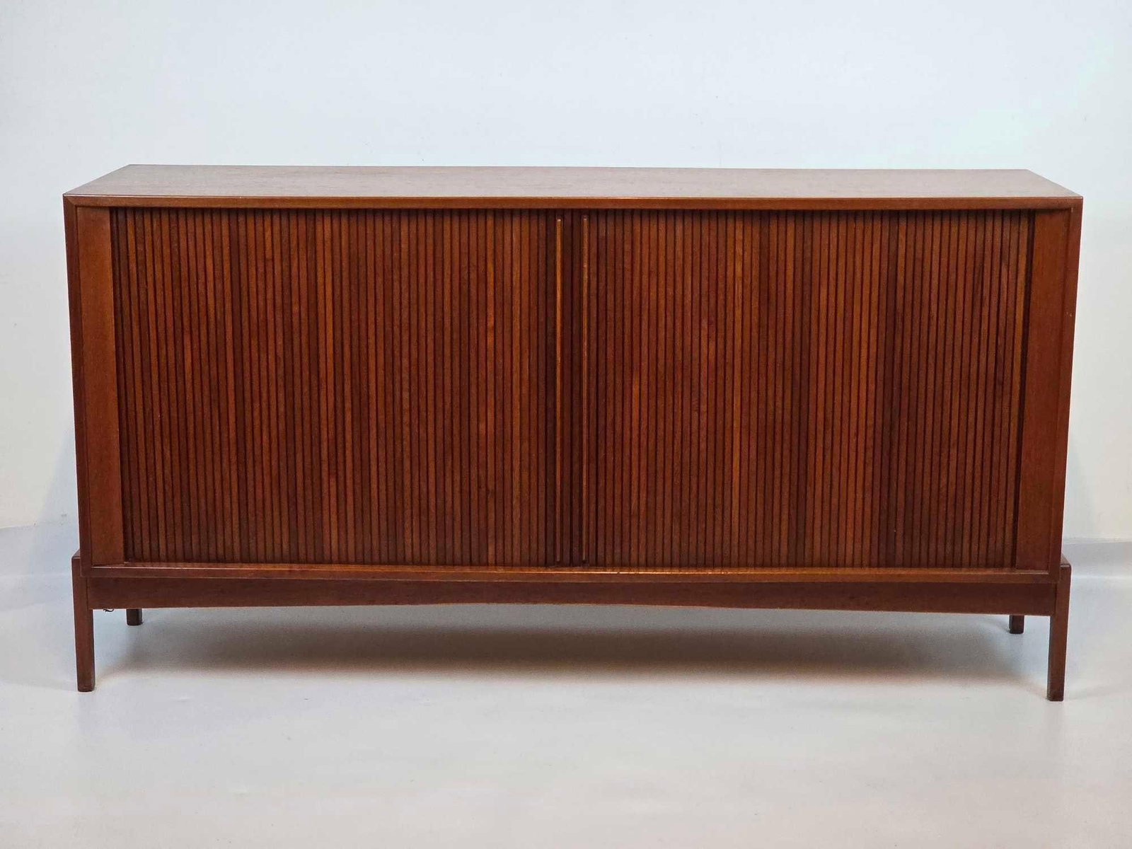 DUX STYLE MID CENTURY WALNUT TAMBOUR DOOR CREDENZA SIDEBOARD: Mid-century modern walnut credenza with twin full-length slatted tambour sliding doors, divided interior storage, and slender integrated square-tapered legs Approximate Dimensions: 31" H X 59"