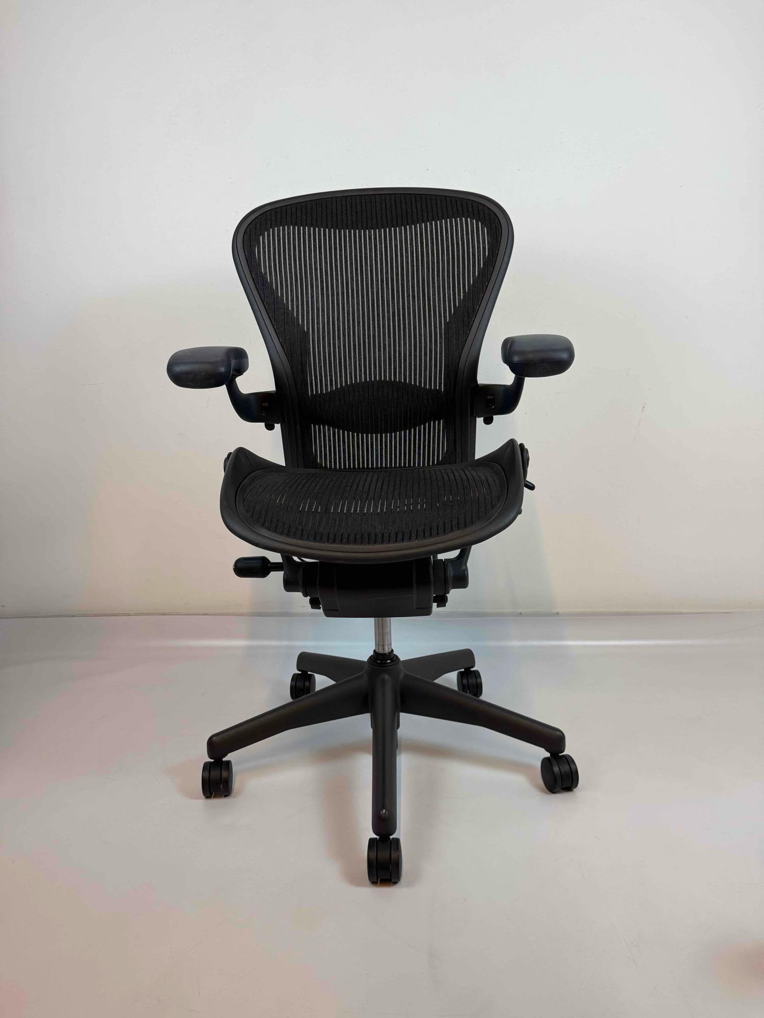 HERMAN MILLER AERON ERGONOMIC BLACK MESH OFFICE DESK CHAIR: Black Pellicle mesh ergonomic swivel desk chair with adjustable arms, posturefit back support, and caster base Approximate Dimensions: 45” H X 28” W X30” D Artist or Maker: Herman Mi
