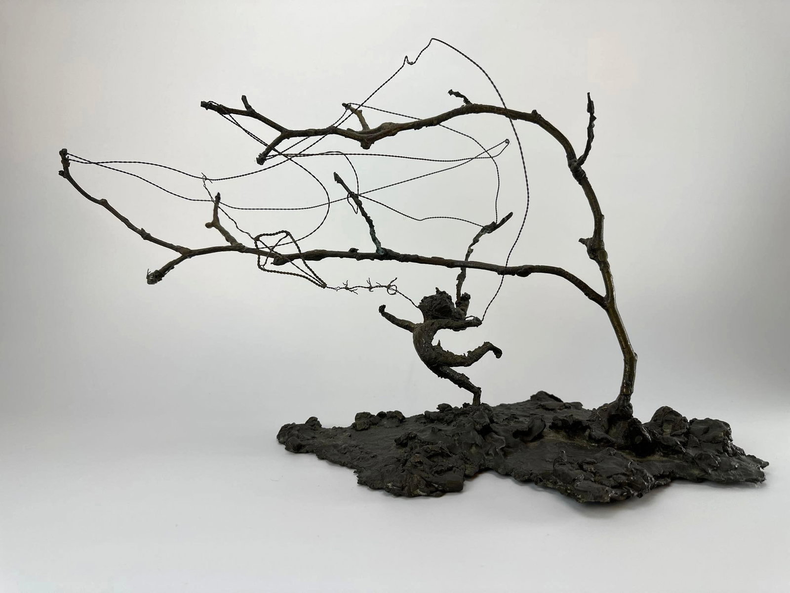 BRONZED BRUTALIST WIRE SCULPTURE, WINDSWEPT TREE WITH FIGURE: Bronzed wire and metal sculpture of a windswept tree with a small figure, on a naturalistic textured base Approximate Dimensions: 19" H x 12" W x 10" D Artist or Maker: Unknown Provenance: