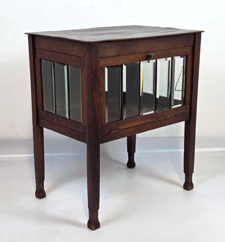 ART NOUVEAU DUTCH OAK TEA CABINET WITH BEVELED GLASS AND DROP FRONT: Oak tea cabinet on tapered legs with beveled glass side panels and a drop-front door over a lower shelf. Approximate Dimensions: 25.25" H X 21.75" W X 15" D Artist or Maker: Unknown Proven