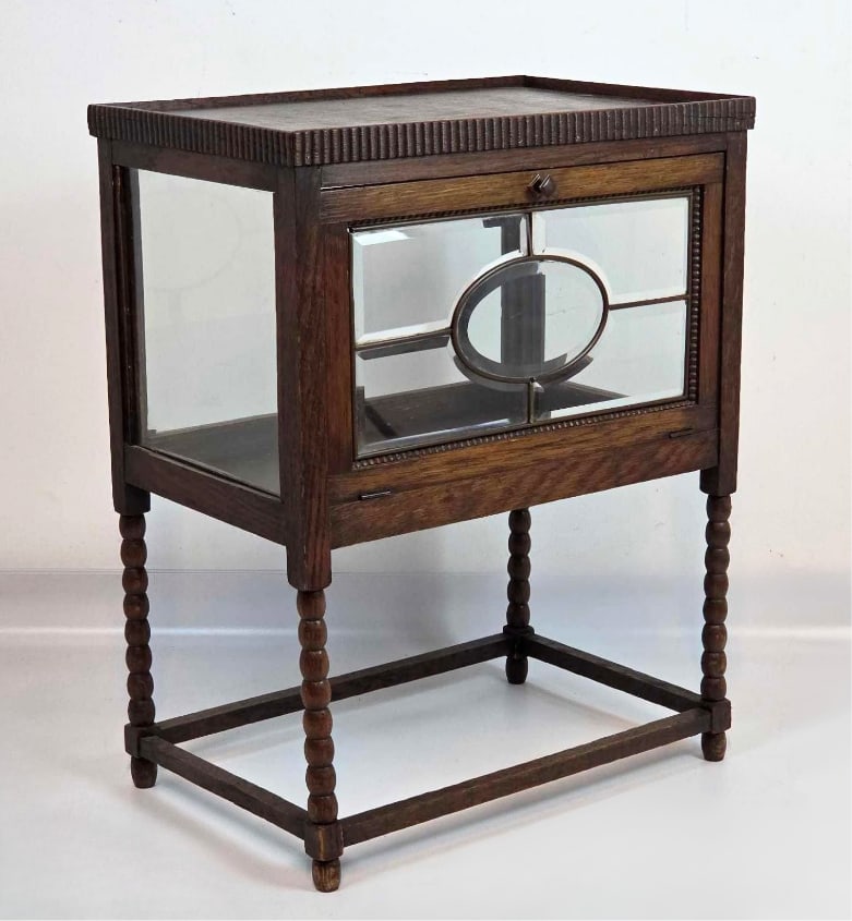 ART NOUVEAU OAK TEA CABINET WITH BEVELED GLASS DROP FRONT: Oak tea cabinet with beveled leaded-glass panels centered by an oval motif, drop-front door, and lower shelf. Approximate Dimensions: 28" H X 22" W X 14.5" D Artist or Maker: Unknown