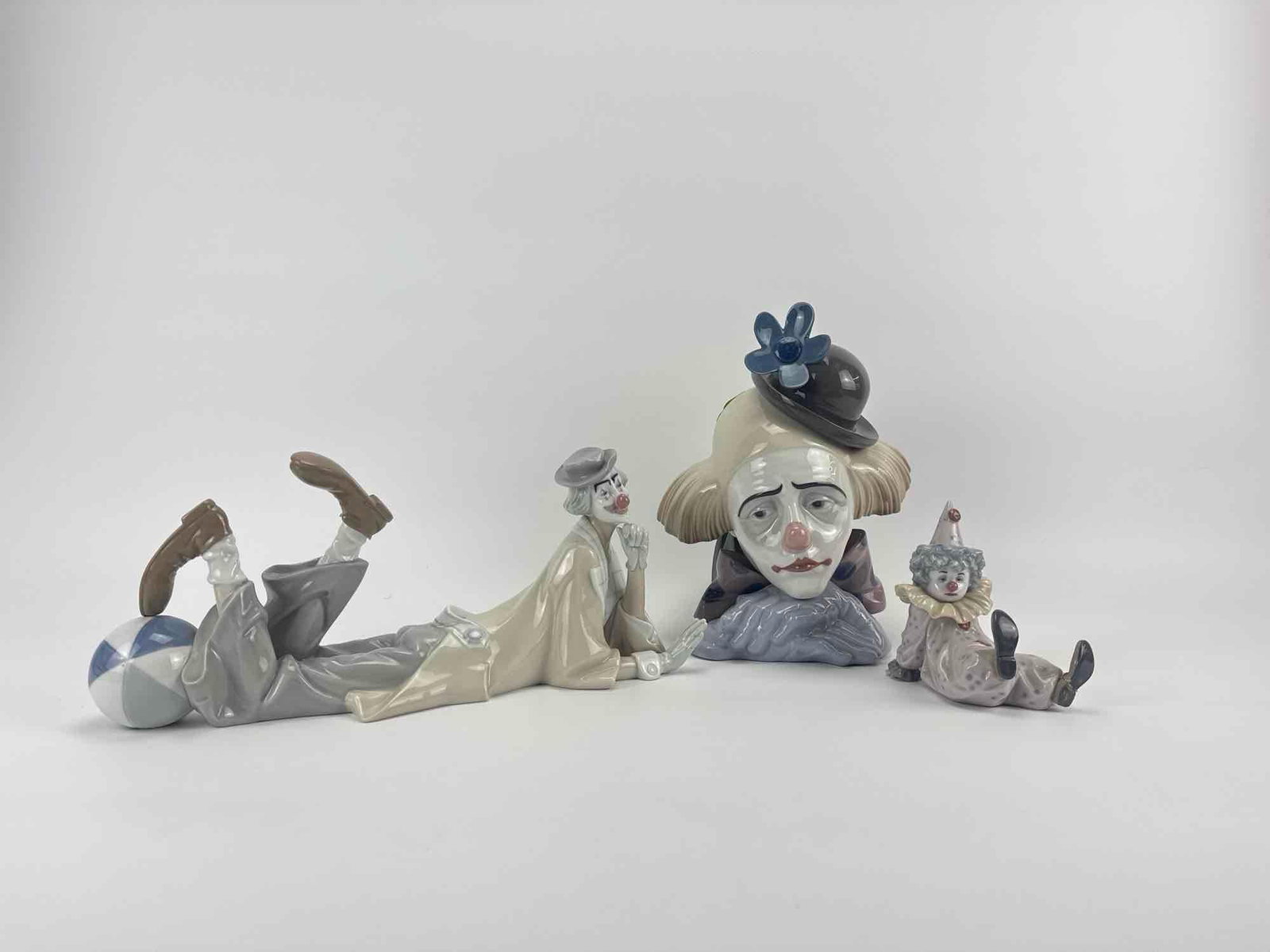THREE LLADRO PORCELAIN CLOWN FIGURINES: Three Lladro glazed porcelain reclining and bust clown figurines with blue backstamps, one with restoration to neck. Approximate Dimensions: 11" H x 8" W x 7.5" D tallest Artist or Maker: 