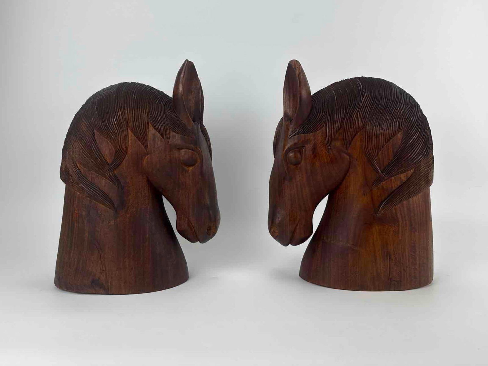 PAIR CARVED WOOD HORSE HEAD SCULPTURES: Pair of carved and stained wood horse head sculptures with well-defined manes Approximate Dimensions: 14" H x 5.5" W x 10.5" D each Artist or Maker: Unknown – carved hardwood Provenance: