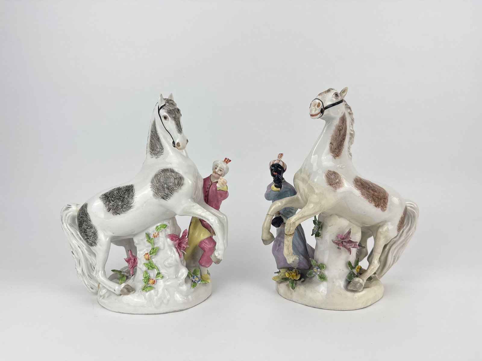 PAIR OF MEISSEN PORCELAIN HORSE-AND-ATTENDANT FIGURE GROUPS, GERMAN, LATE 19TH/EARLY 20TH C.: Pair of polychrome porcelain groups, each a spotted rearing horse with a companion figure and applied flowers on a scrolled base. Note repairs in photos. Approximate Dimensions Each: 9" H X 7.5