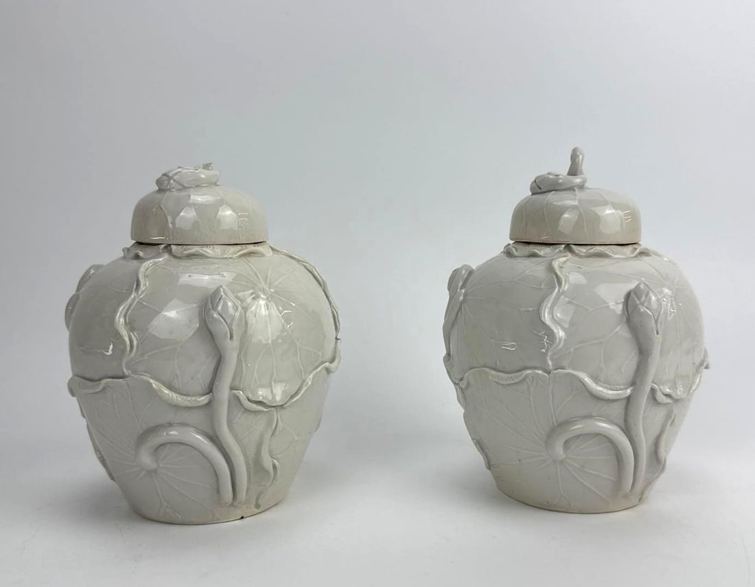 PAIR OF WHITE PORCELAIN LILY-PAD GINGER JARS, ASIAN: Pair of small white-glazed covered ginger jars with molded lily pads, flowers, and frog accents. Note loss to lid on left. Approximate Dimensions: 6.5" H X 5.25" Dia. Artist or Maker: Unknown 