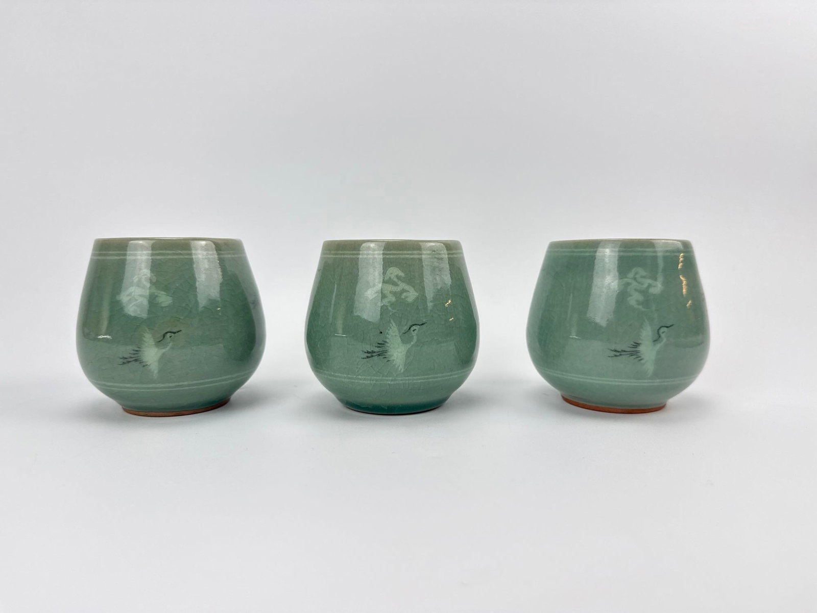 SET OF THREE GREEN CRACKLE CELADON TEACUPS: Set of three celadon-green crackle-glaze teacups with exposed stoneware footrings. Approximate Dimensions Each: 3" H X 3.25" Dia. Artist or Maker: Unknown; celadon-glazed stoneware, Asian Prov