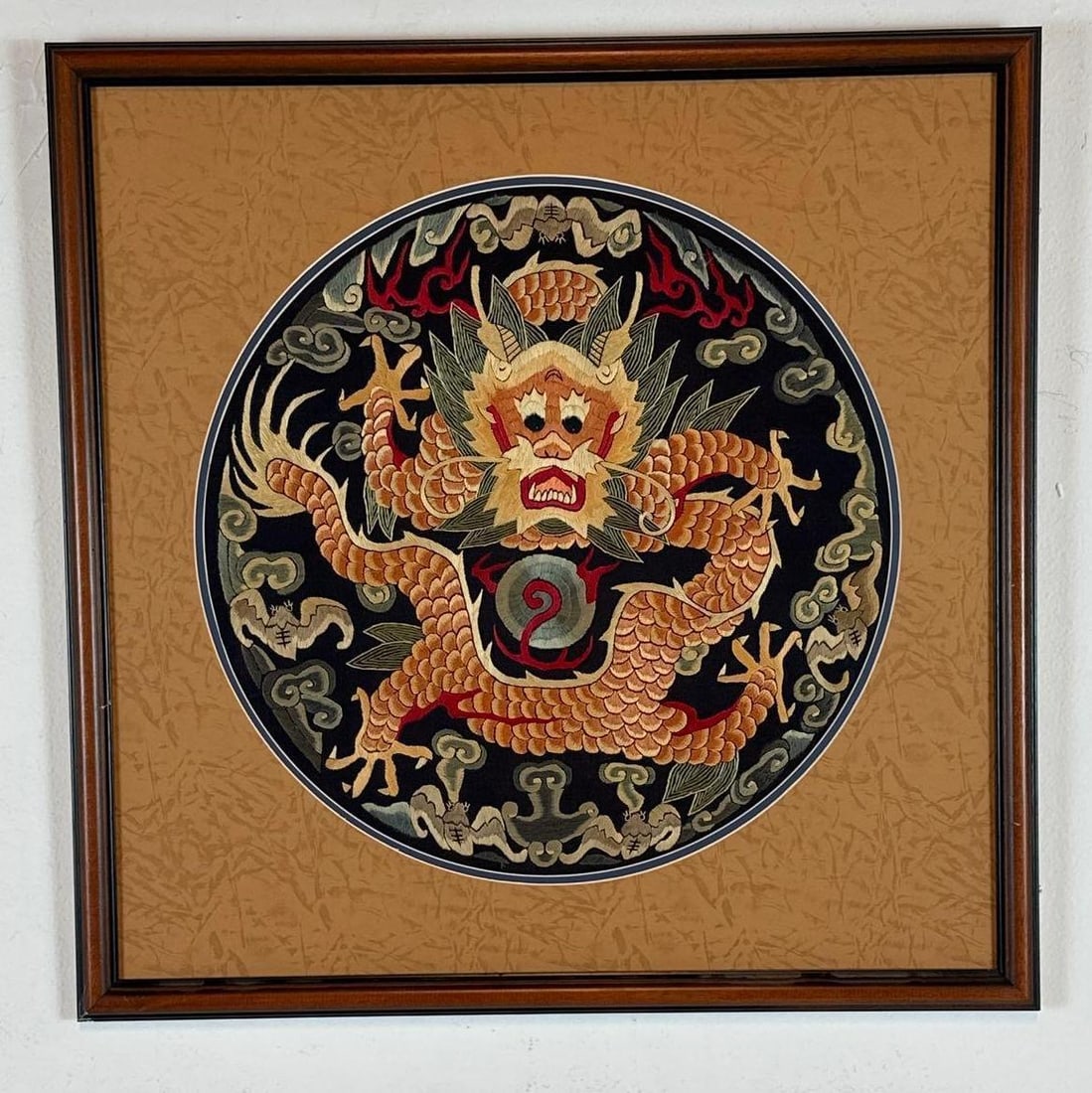 CHINESE SILK EMBROIDERED DRAGON ROUNDEL, FRAMED: *Chinese silk embroidered dragon roundel in the style of an imperial rank badge, depicting a five-clawed dragon amid cloud and bat motifs on a dark ground, in a wood frame. Approximate Dimensions: Pan