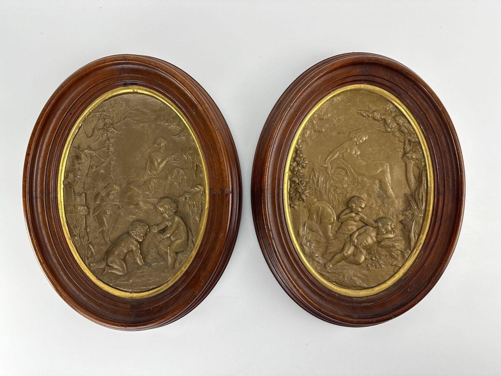 PAIR FRENCH NEOCLASSICAL BRONZE BAS-RELIEF OVAL PLAQUES IN WOOD FRAMES: *Pair of 19th-century French Neoclassical oval patinated bronze bas-relief panels depicting allegorical nymphs and playing putti mounted in gilt-trimmed carved wooden frames. Approximate Dimensions: 1