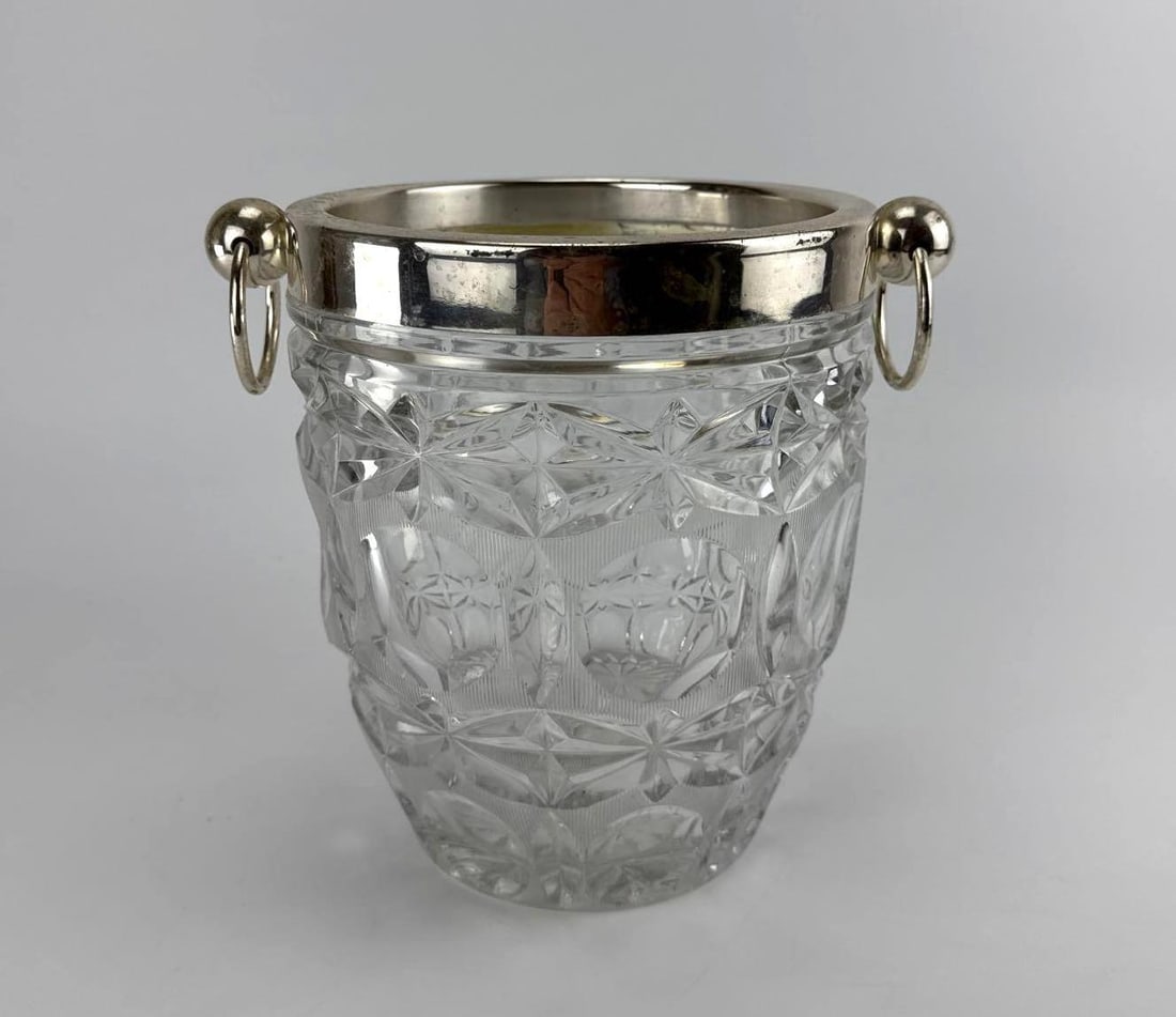 GERMAN CUT CRYSTAL CHAMPAGNE BUCKET WITH SILVER PLATED RIM AND DROP HANDLES: *Deeply cut lead crystal champagne cooler with a silver plated collar rim and dual drop ring handles. Approximate Dimensions: 8” dia x 9” T Artist or Maker: Unknown Proven