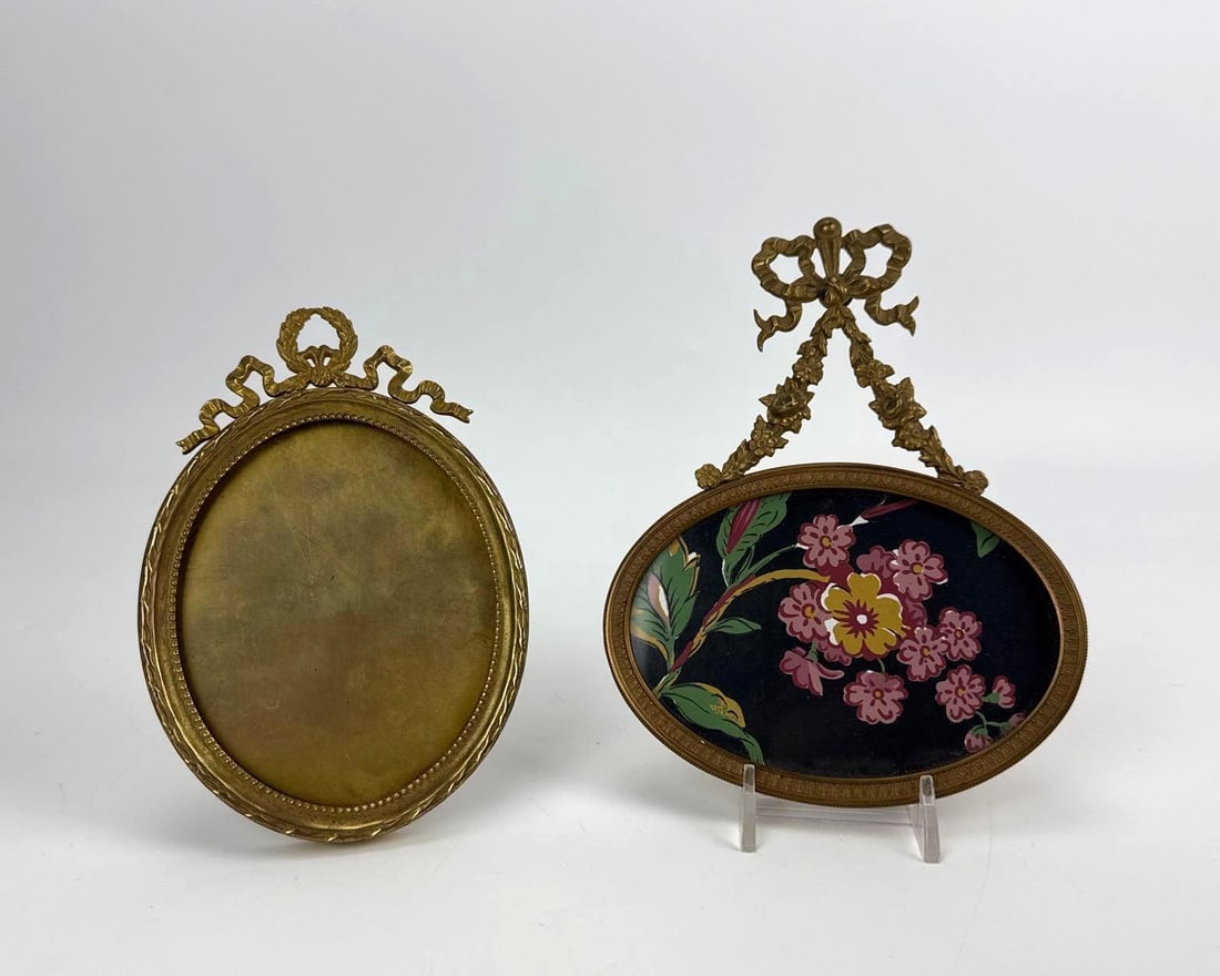 TWO ANTIQUE OVAL NEOCLASSICAL BRONZE FRAMES: Two antique oval bronze frames, one with a hand-painted floral panel Approximate Dimensions: taller 7" H x 5" W x 0.5" D Artist or Maker: Unknown; gilt bronze with ribbon crest Provenance: