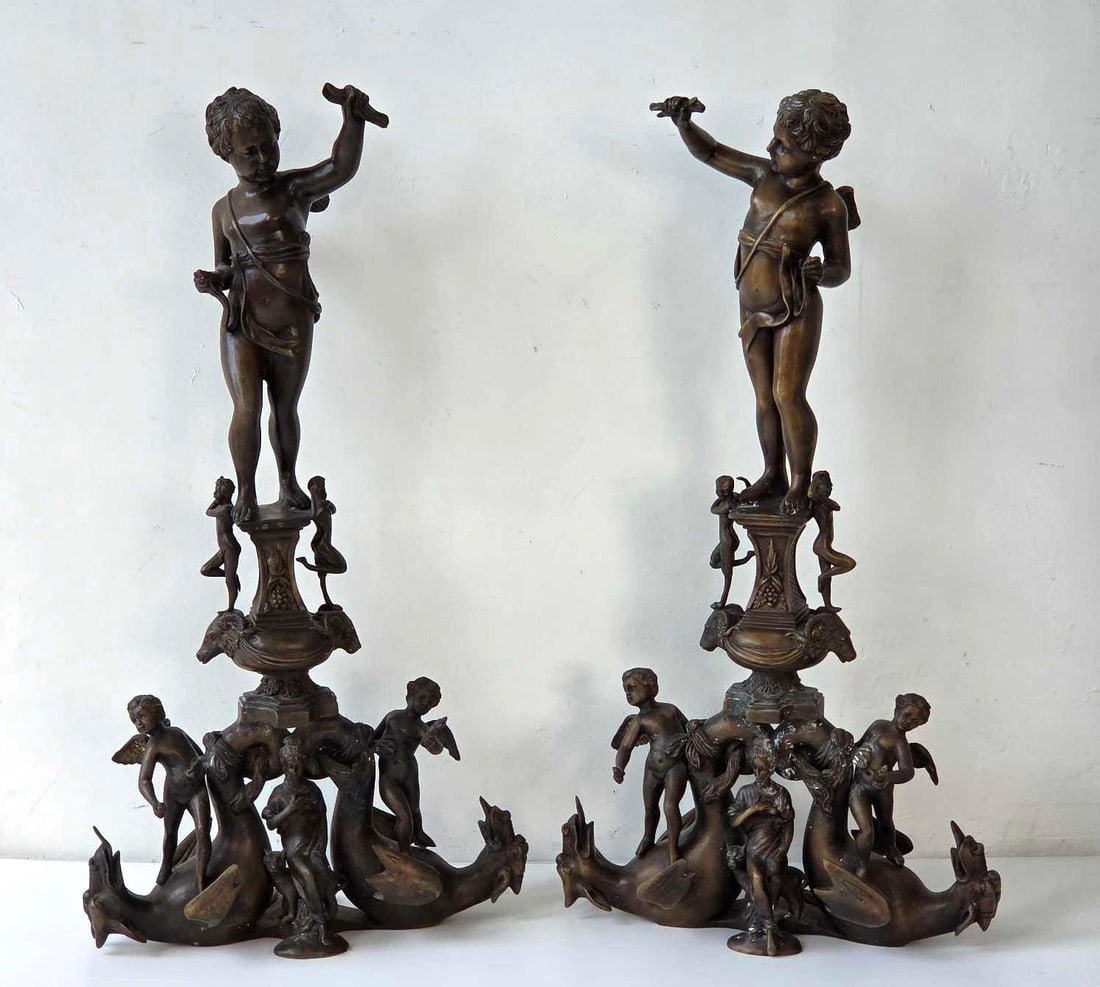 PAIR OF FIGURAL BRONZE CHENETS WITH PUTTI AND MERMAIDS: Pair of figural bronze chenets, each with a winged putto atop an urn on a base of mermaids and dolphins. Approximate Dimensions Each: 32.5" H X 18" W X 7" D Artist or Maker: Unknown Proven