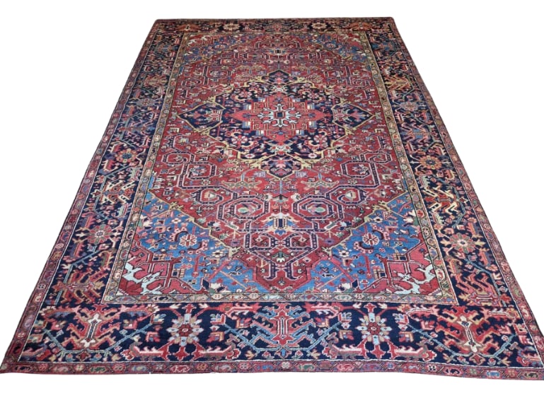 PERSIAN HERIZ HAND KNOTTED WOOL RUG: Persian Heriz hand-knotted wool rug featuring a large stepped medallion in blue and ivory on a rose-red field, framed by a navy-blue floral border with allover geometric floral motifs Approximate Dime