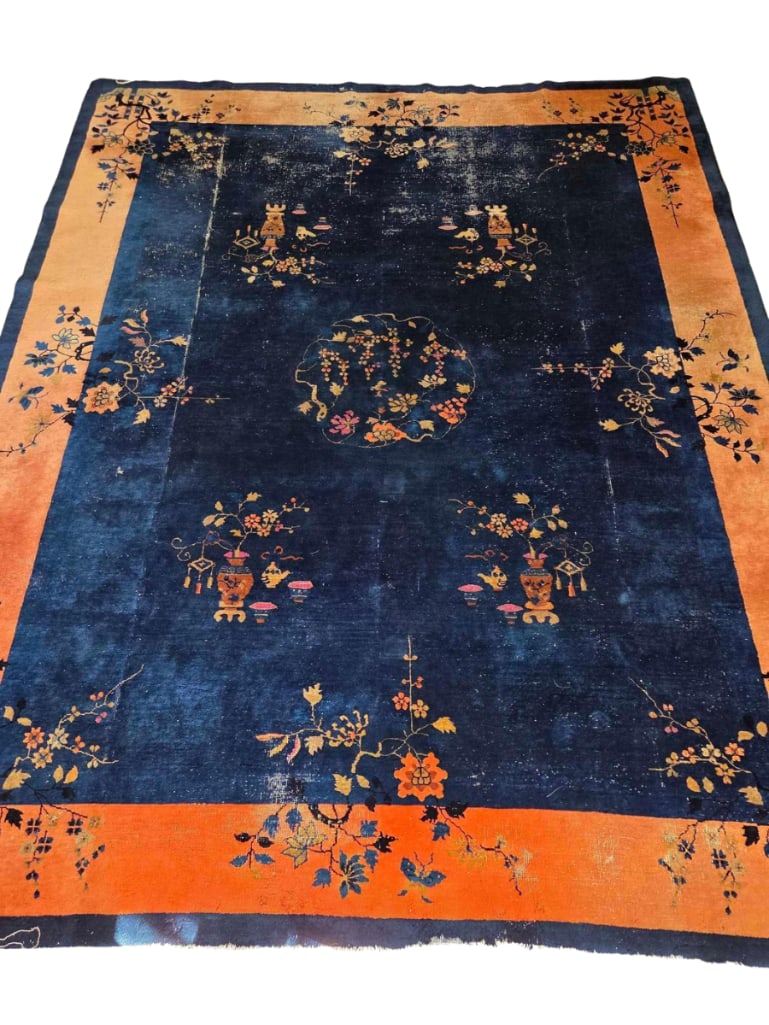 ANTIQUE CHINESE ART DECO HAND KNOTTED WOOL RUG: Antique Chinese Art Deco hand-knotted wool rug with scattered floral sprays and vase-and-precious-objects motifs on an indigo-blue field, enclosed by a wide salmon-apricot border; showing age-appropri
