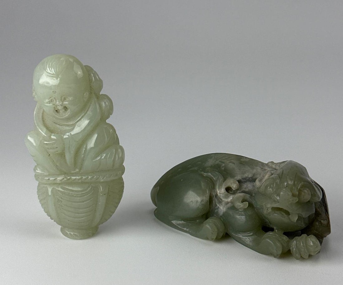 TWO CHINESE CARVED JADE FIGURES, BOY AND RECUMBENT BEAST, CELADON: Two Chinese carved jade figures, a pale celadon standing smiling boy above a ribbed basket, and a mottled green recumbent mythical beast with russet and grey skin inclusions Approximate Dimensions Lar