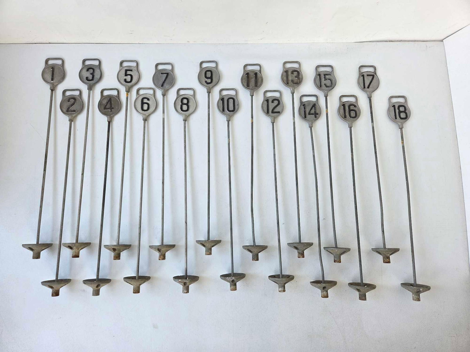 COMPLETE SET OF EIGHTEEN VINTAGE CAST ALUMINUM GOLF HOLE MARKERS, NUMBERED 1 TO 18: Set of eighteen golf course hole markers, each a cast light alloy keyhole-shaped plaque with a raised looped handle over a recessed roundel bearing a black painted numeral, running consecutively 1 thr